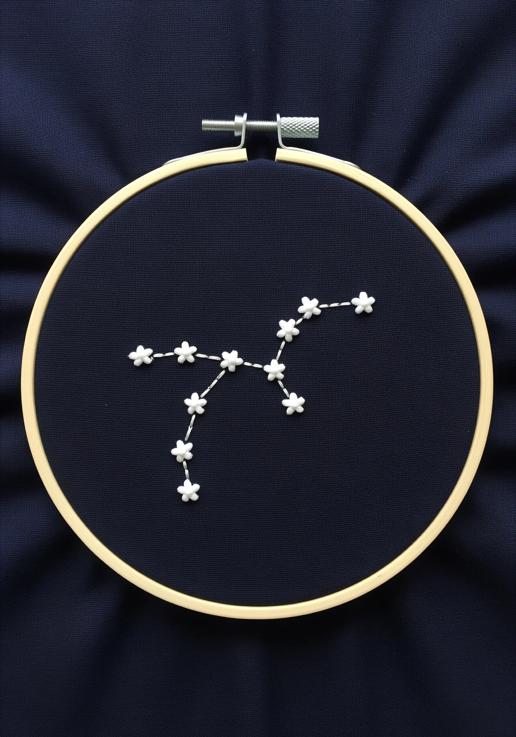 A star constellation made of raised white floral stitches on dark navy fabric in a hoop.