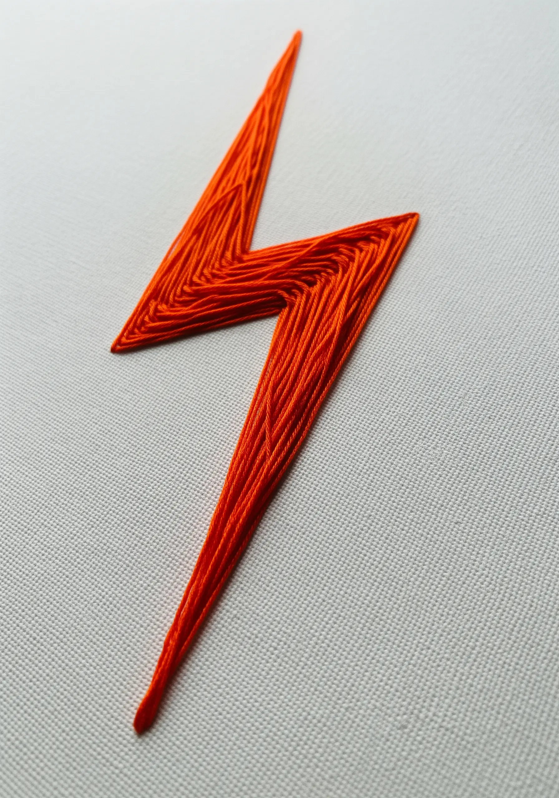 An orange lightning bolt filled with directional satin stitch on a white background.