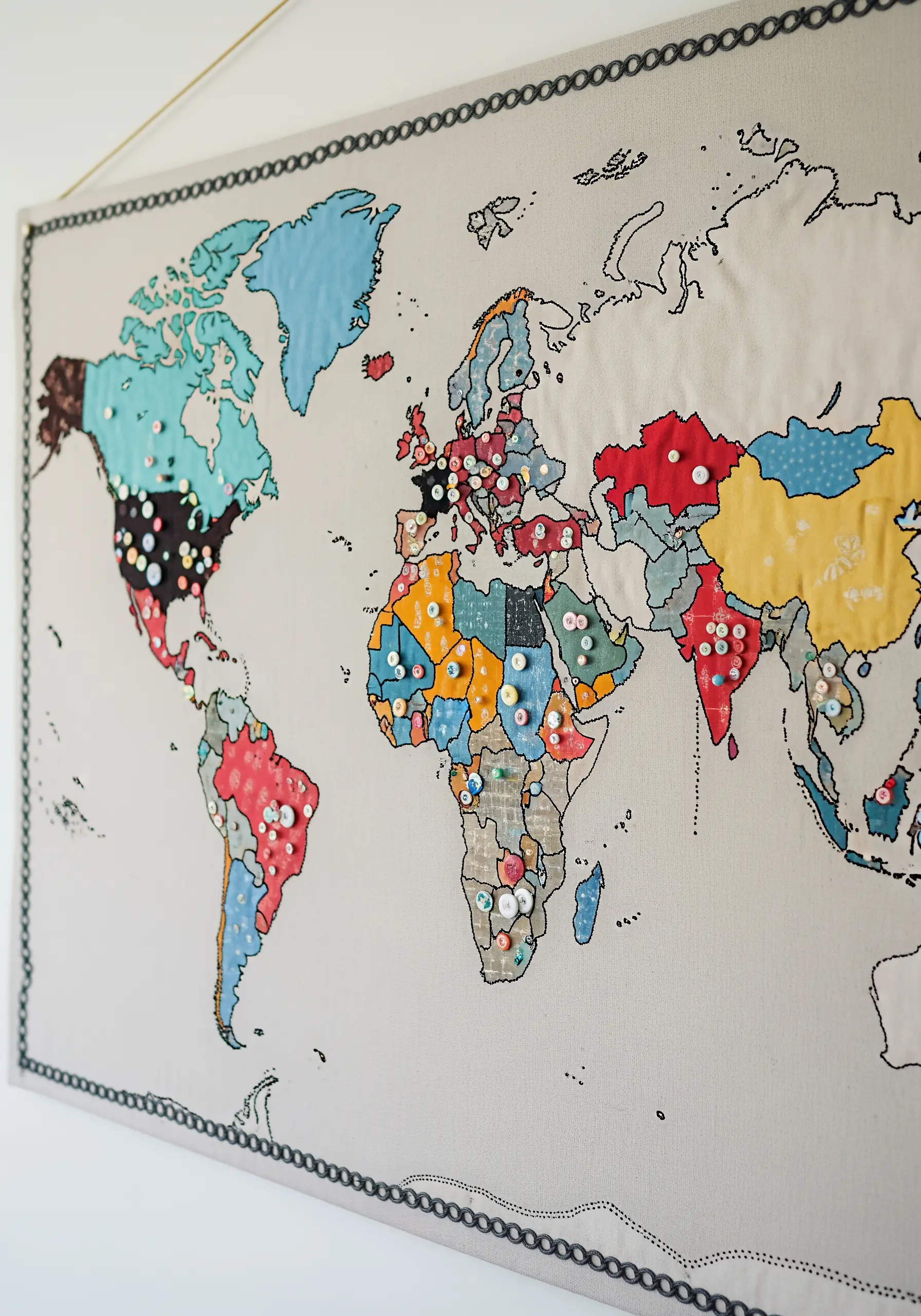 A world map made with fabric appliqué continents, outlined in black stitch, with pins marking locations.