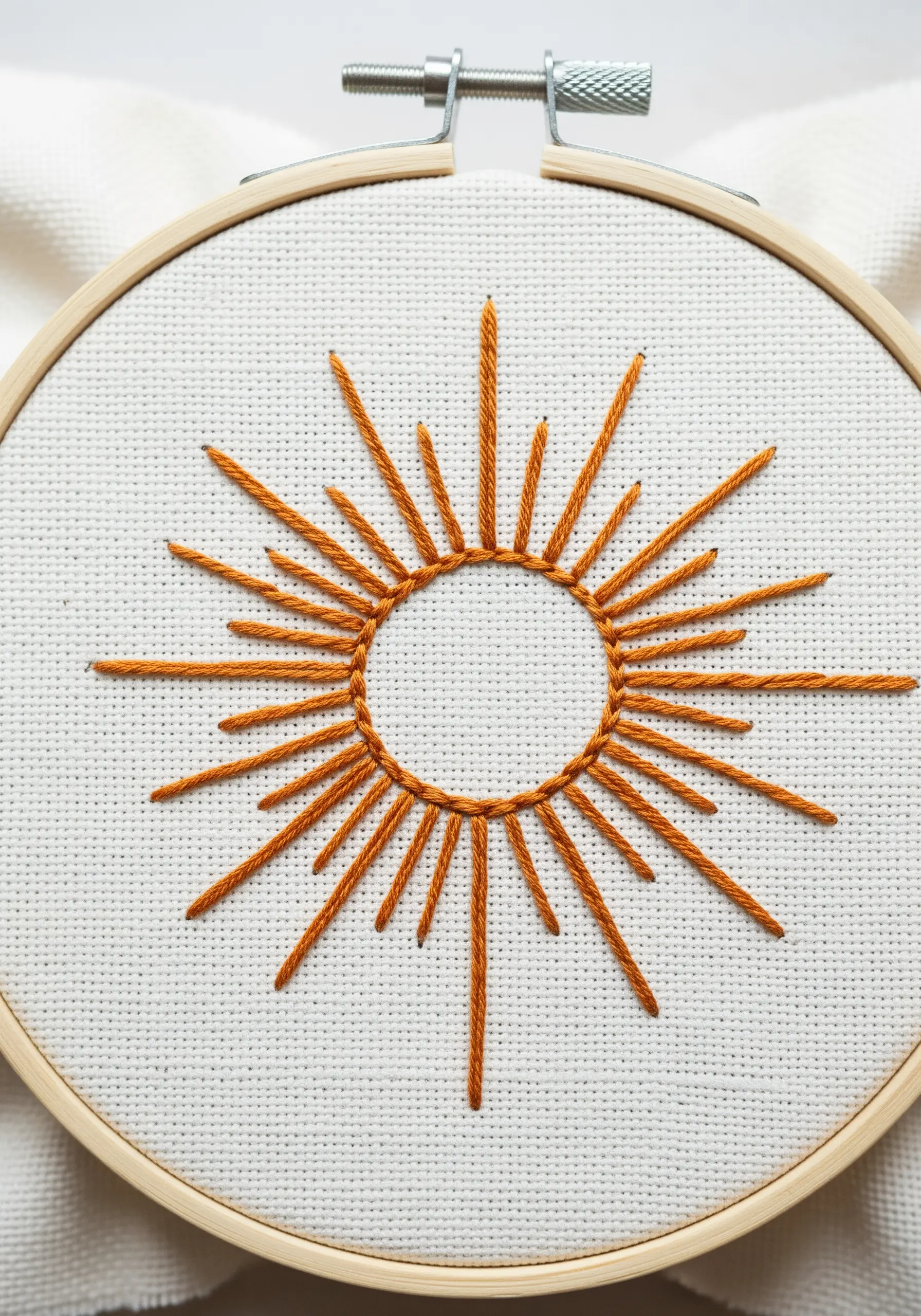 Minimalist sunburst embroidery with long and short straight stitches in orange.