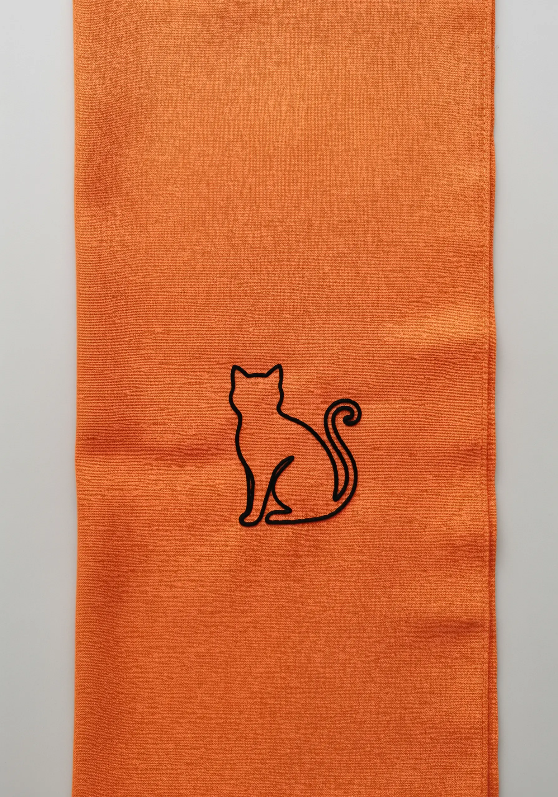 A bold black outline embroidery of a sitting cat silhouette on an orange scarf.