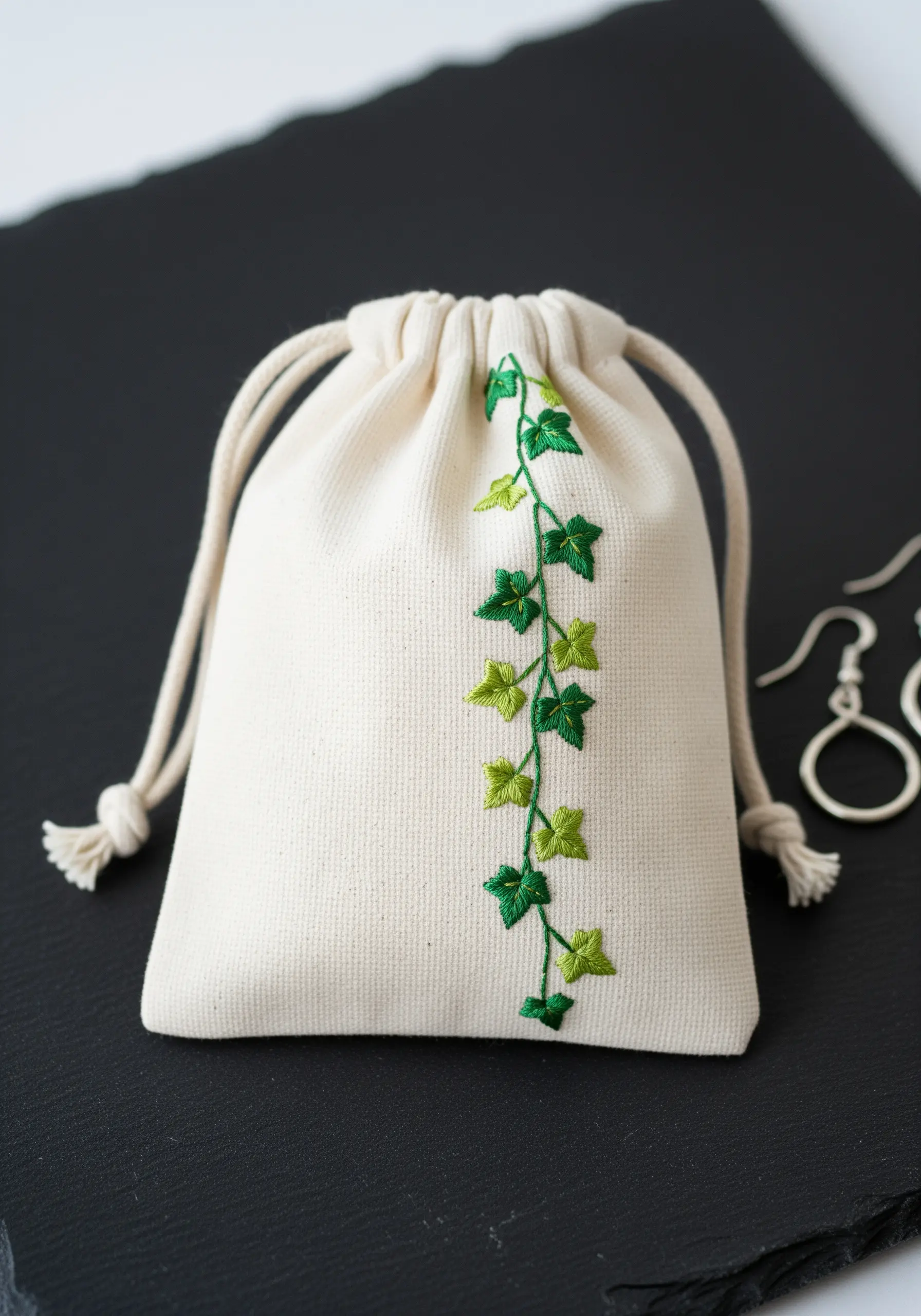 A simple embroidered ivy vine climbing vertically on a small cream drawstring bag.
