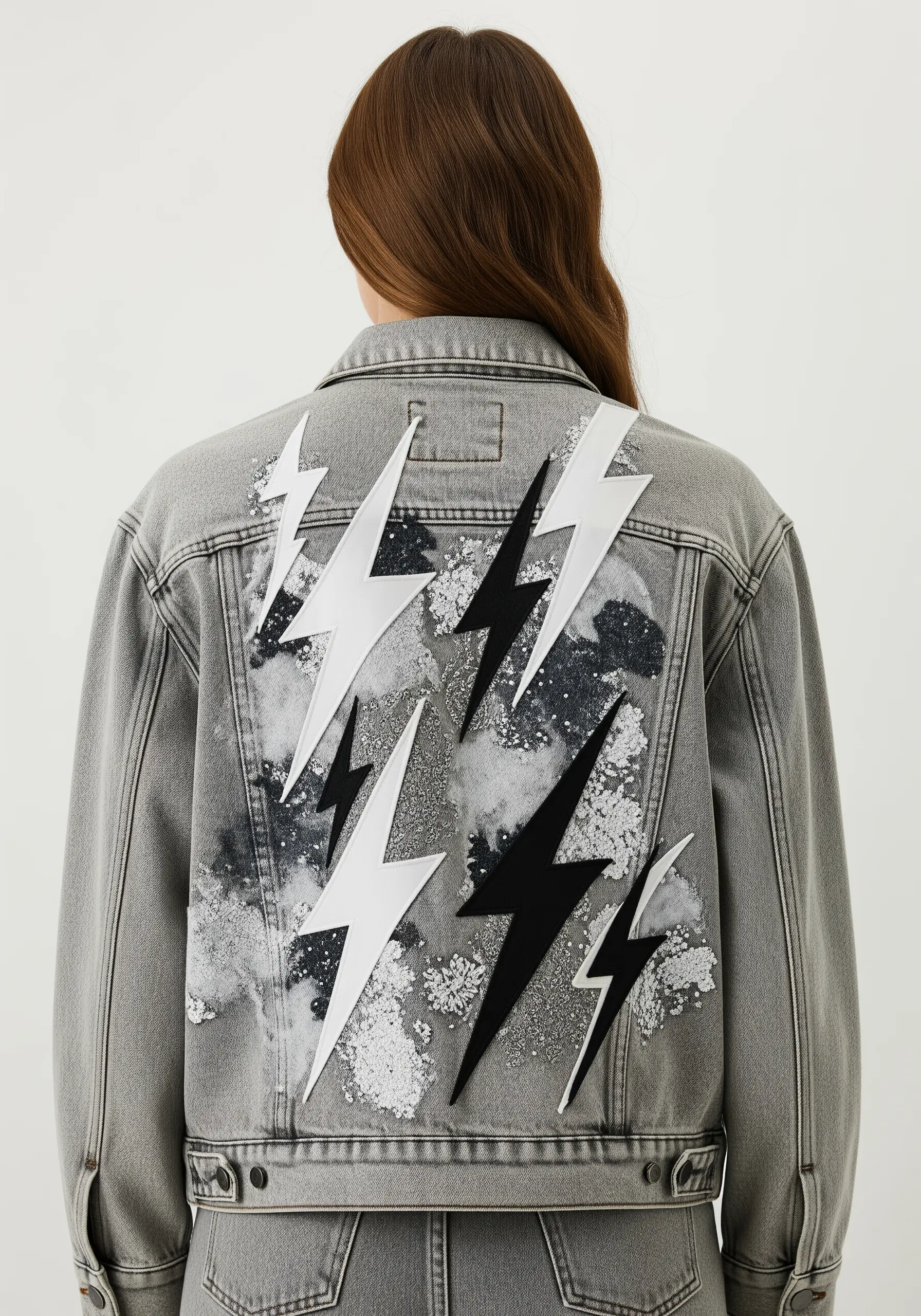 A gray denim jacket embellished with bold black and white leather lightning bolt appliqués.