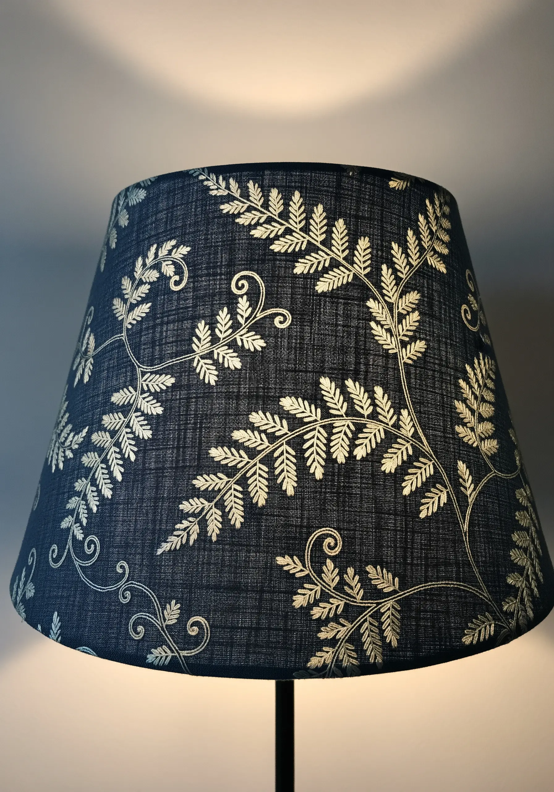 A dark blue lampshade embellished with an elegant pattern of embroidered golden fern leaves.