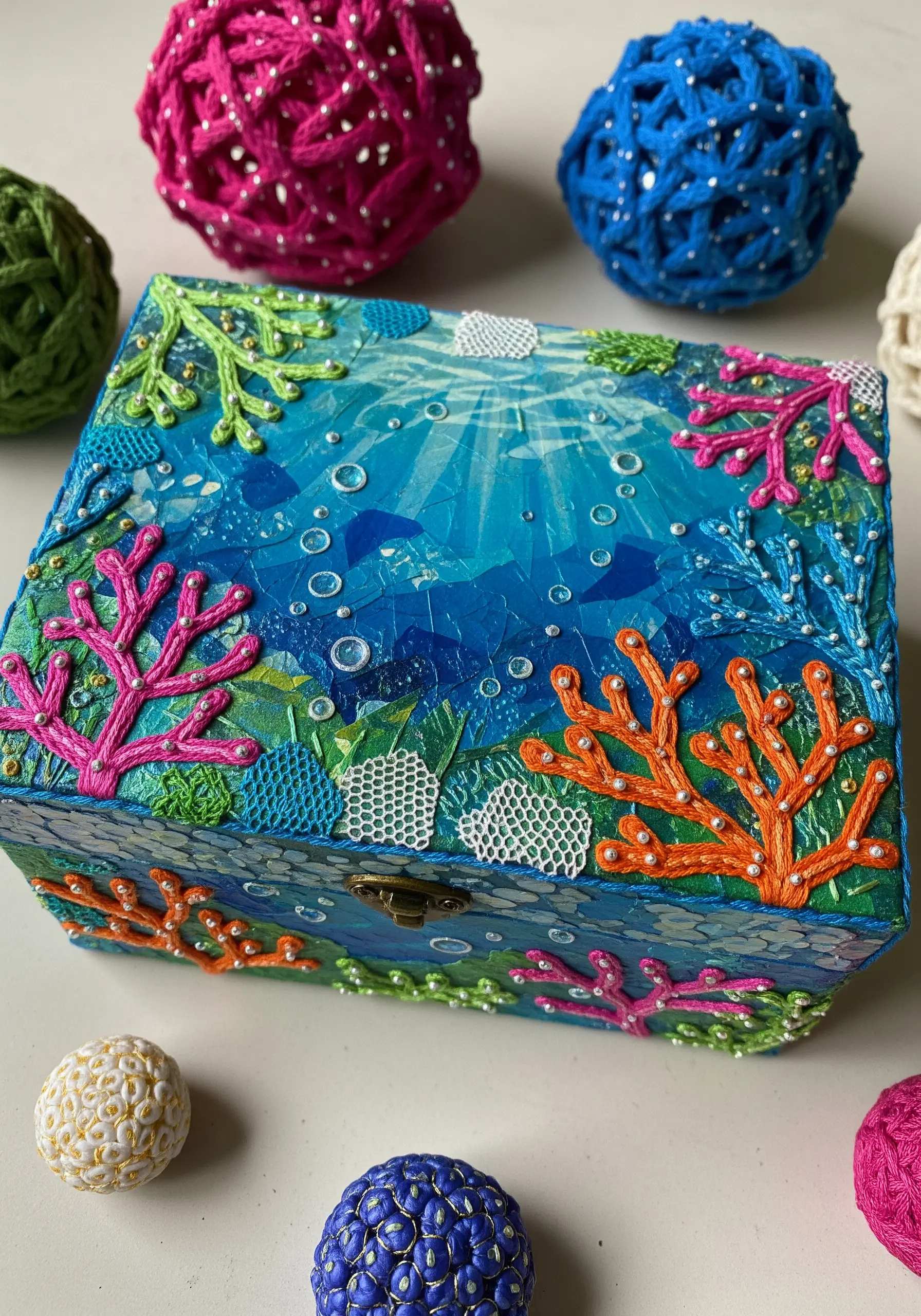 A decorated box with an underwater paper collage, embellished with embroidered coral and French knots.