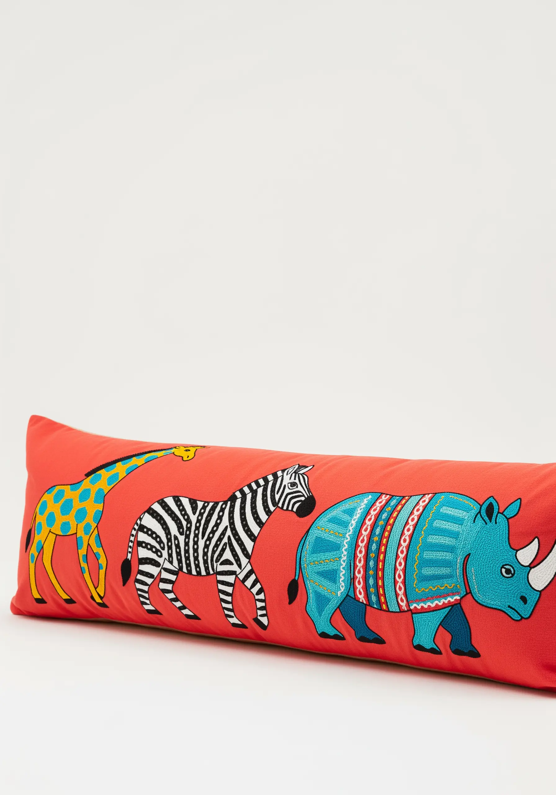 Boldly embroidered giraffe, zebra, and rhino in a colorful parade on a red pillow.