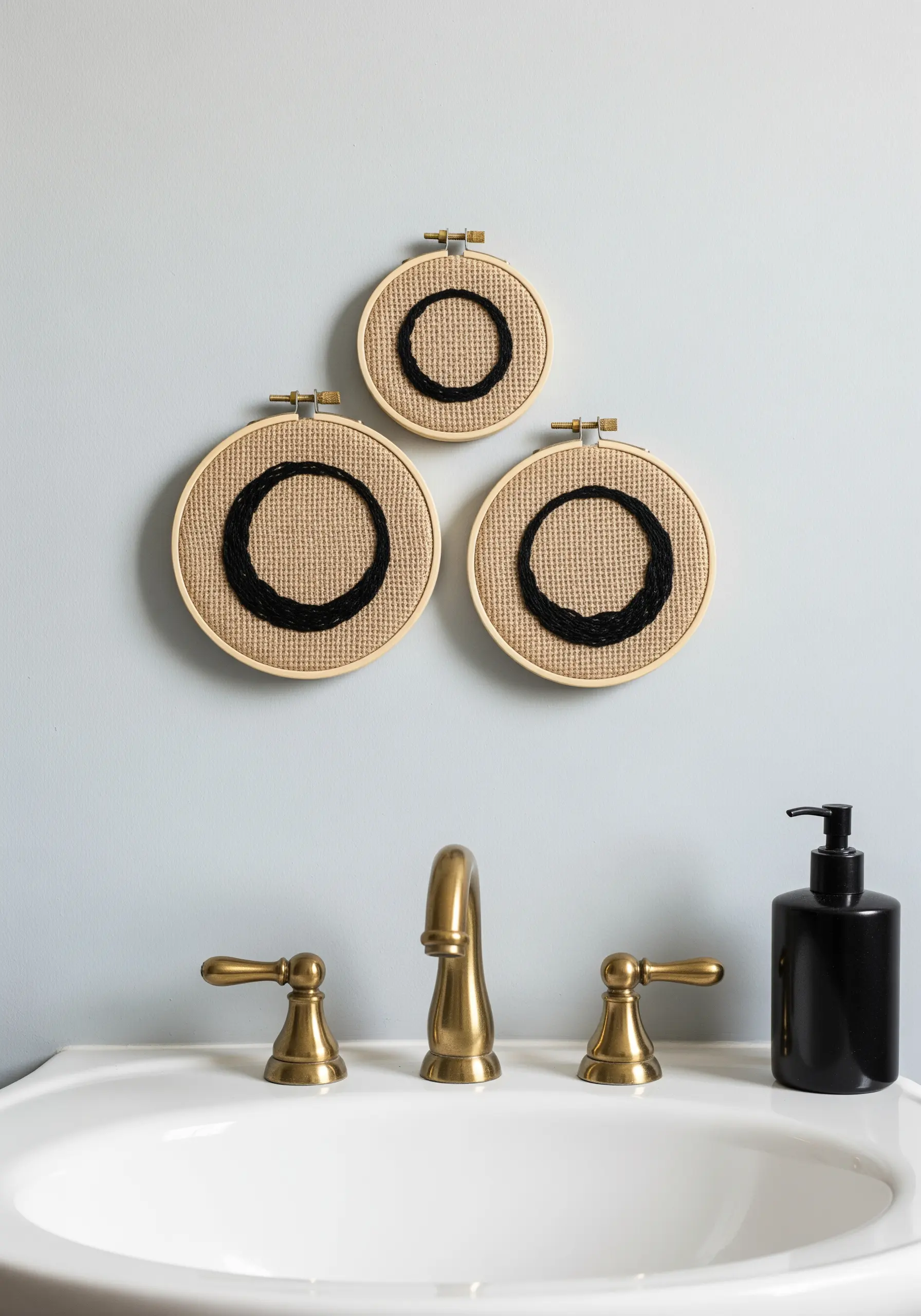 Three embroidery hoops on a bathroom wall with textural black circles stitched on burlap.