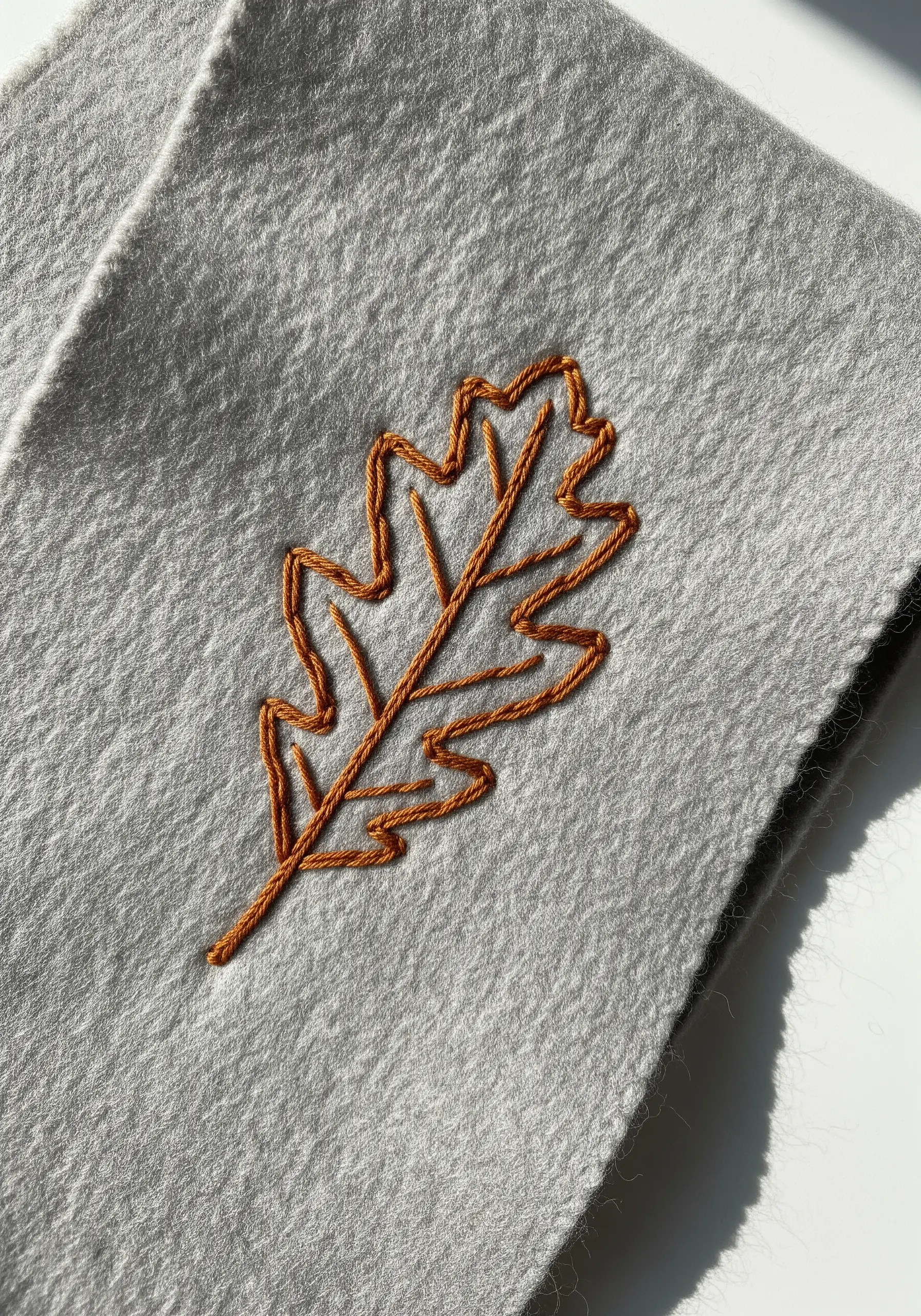 An oak leaf outlined in orange thread on a gray felt scarf.