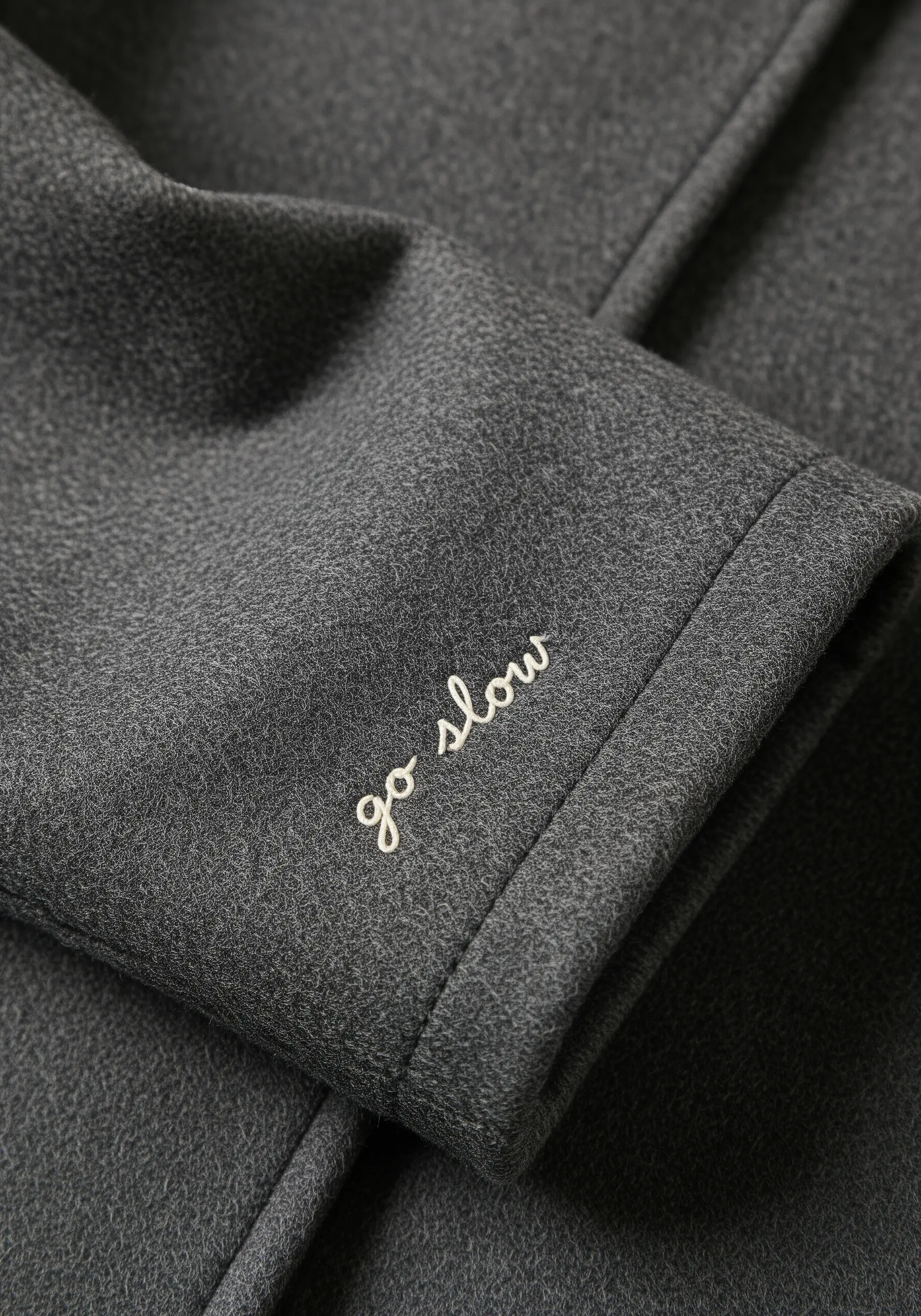 The phrase 'go slow' embroidered in delicate white script on a dark grey coat sleeve.