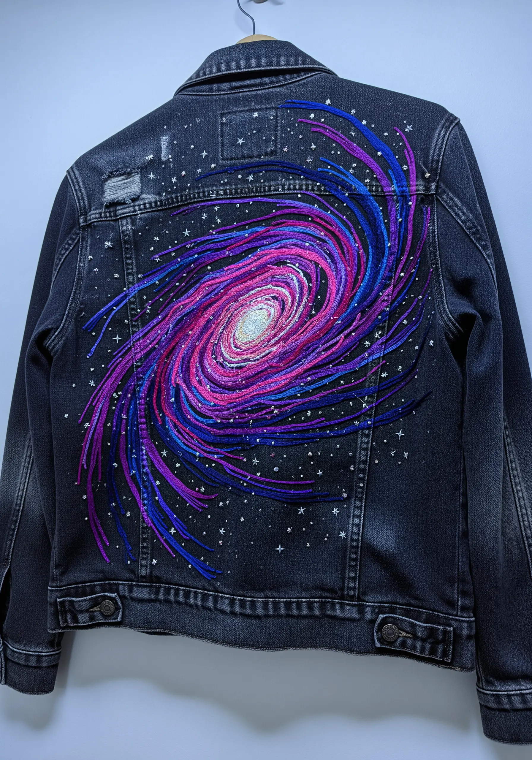 Embroidered spiral galaxy on the back of a black denim jacket.