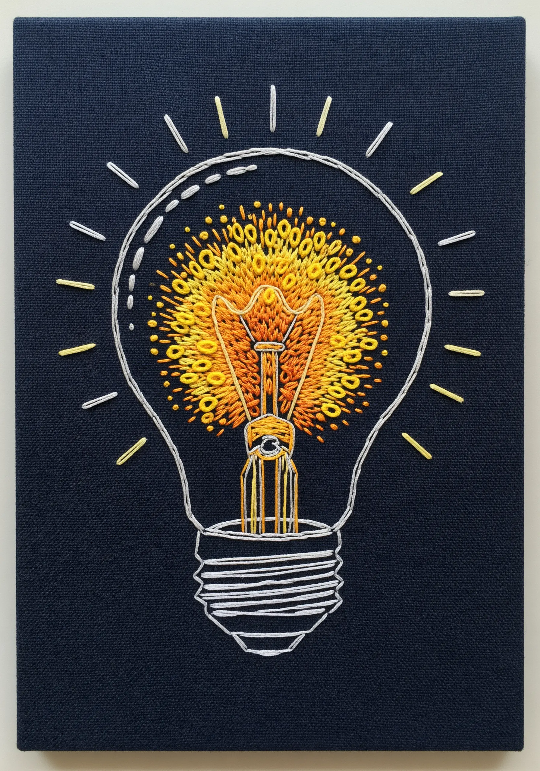 Embroidered lightbulb with a glowing filament made of yellow and orange French knots.