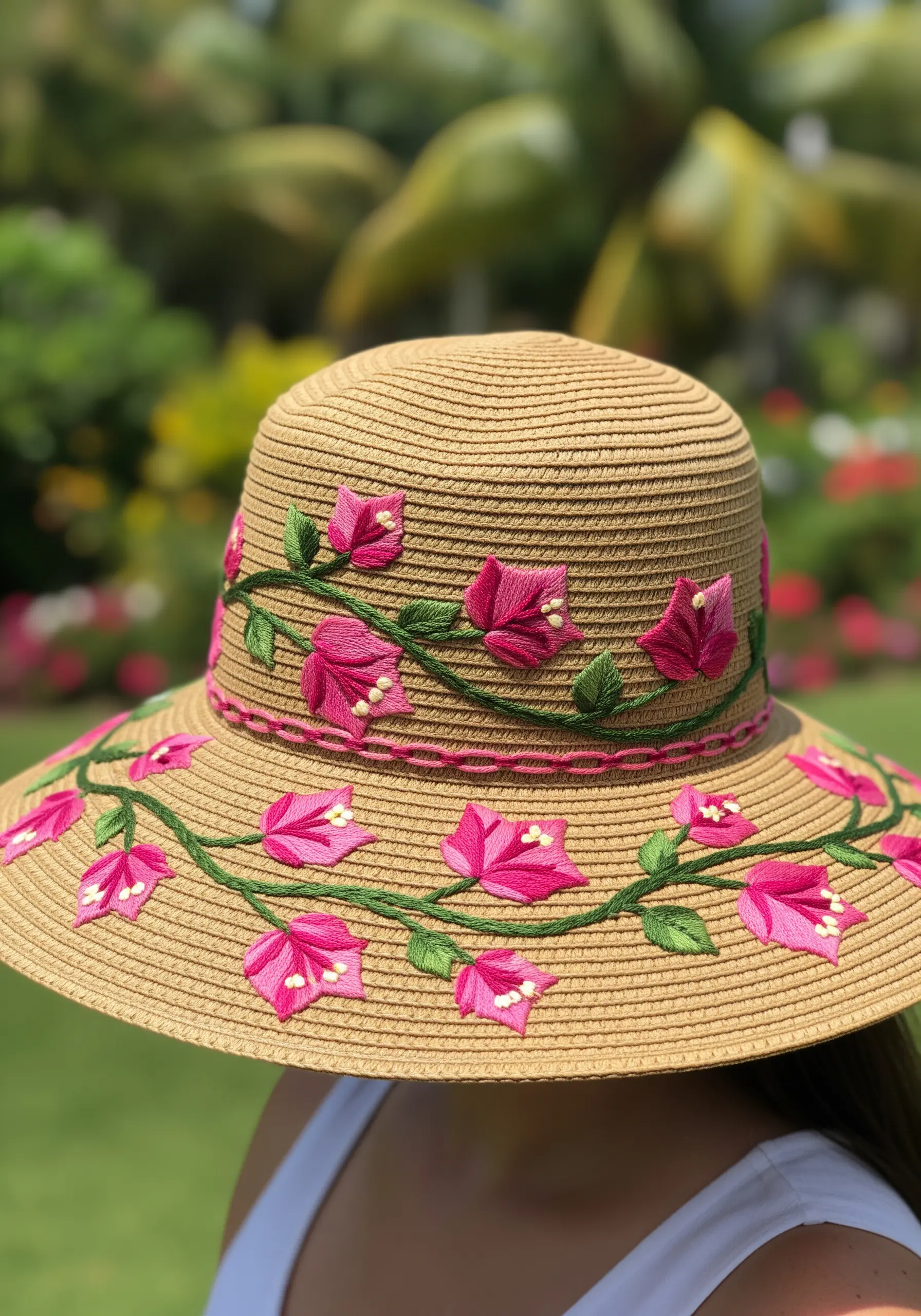 Bright pink bougainvillea vines embroidered around the band of a woven straw sun hat.