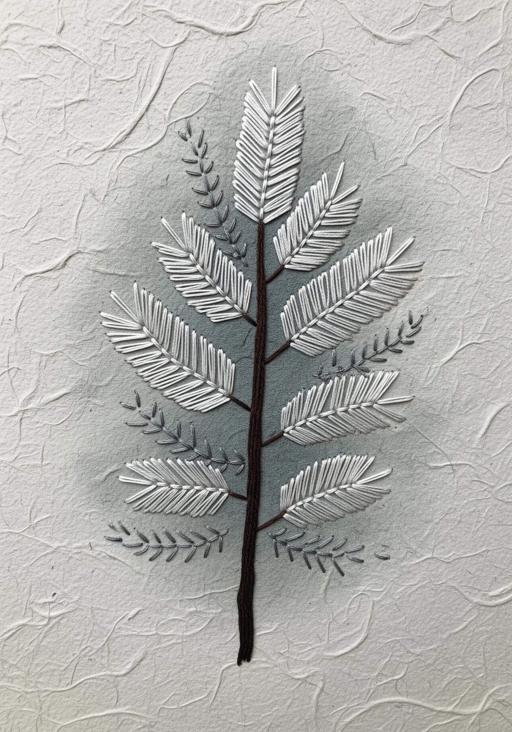 A botanical fern design stitched in white and brown thread on textured gray paper.