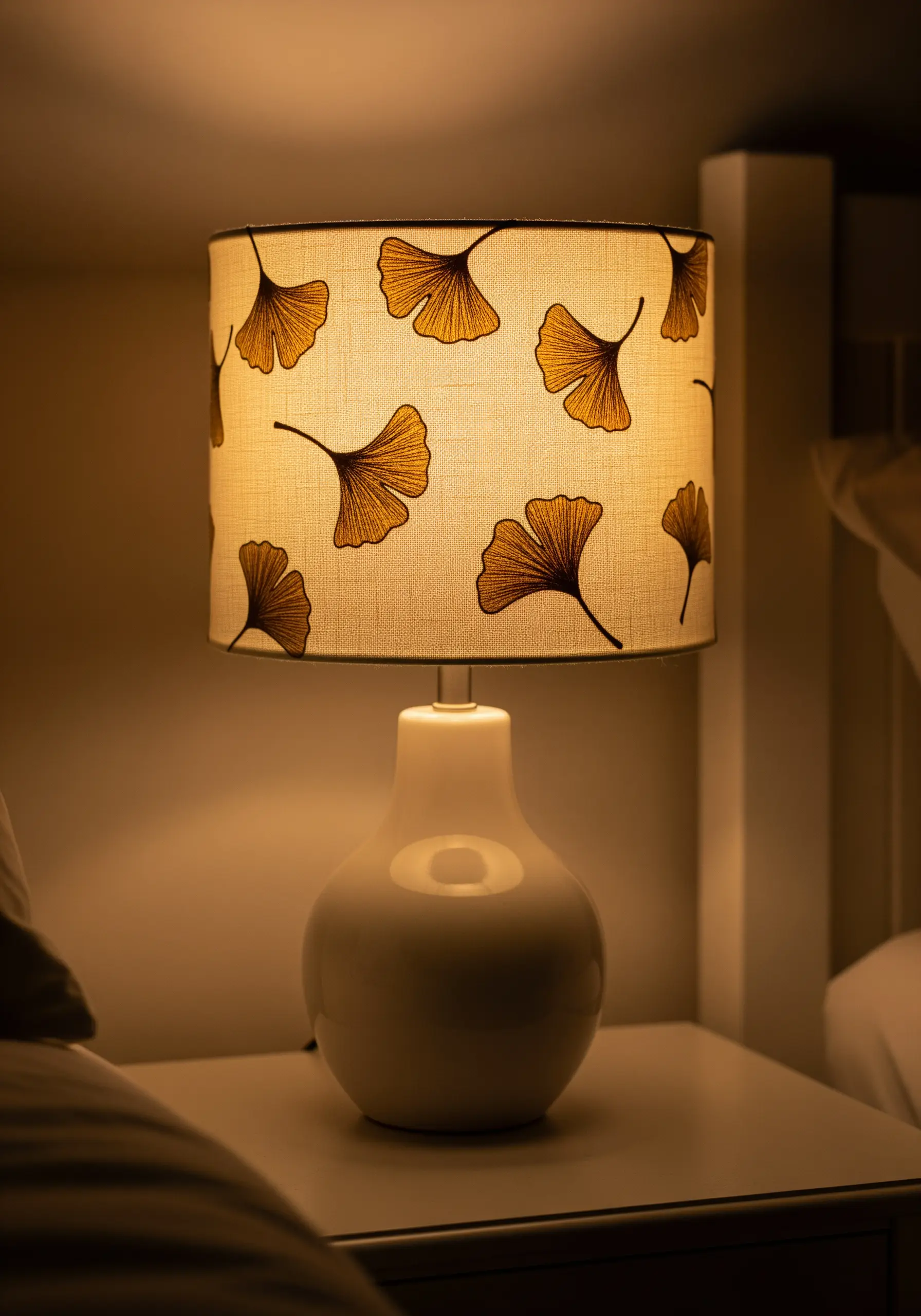 A fabric lampshade with embroidered ginkgo leaves, lit from within.
