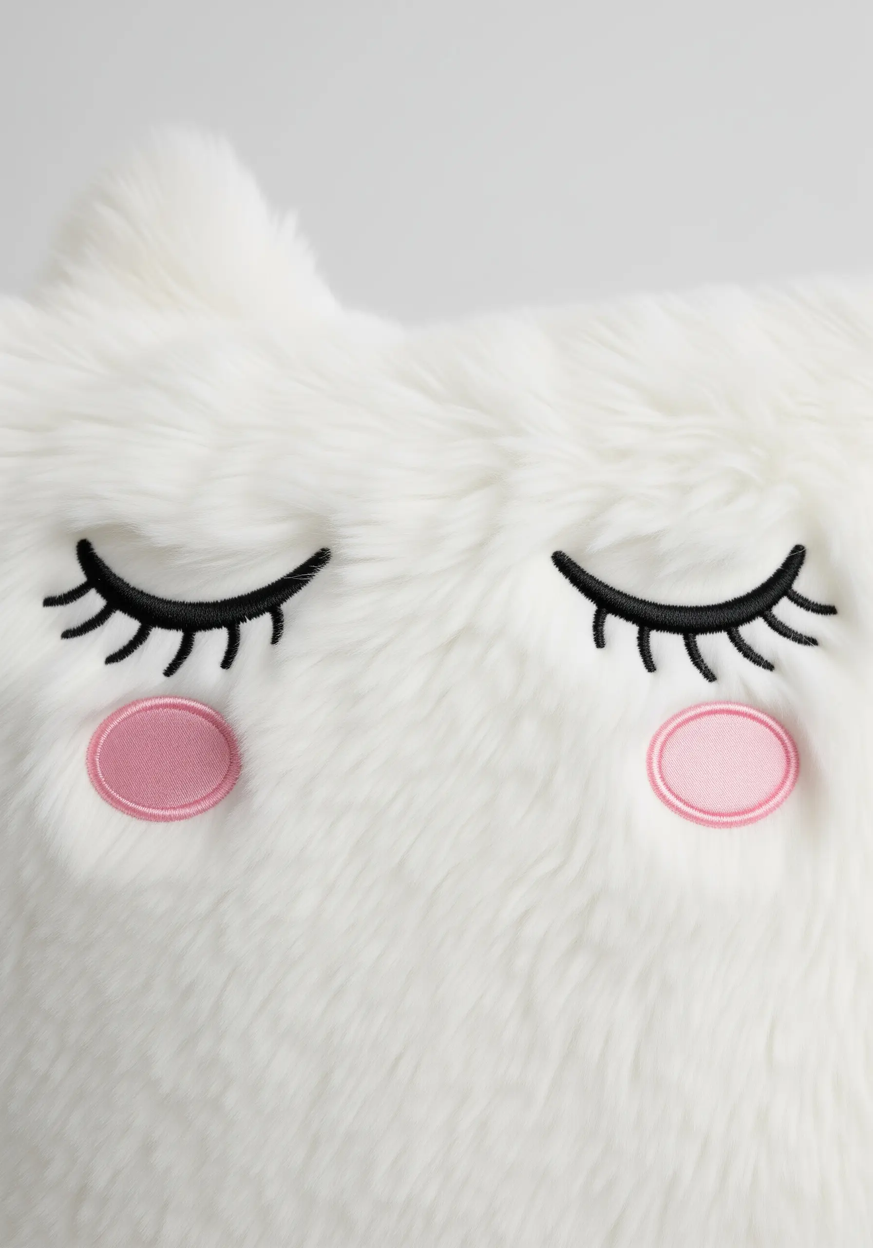 Simple embroidered eyelashes and pink cheeks on a plush white faux fur pillow.