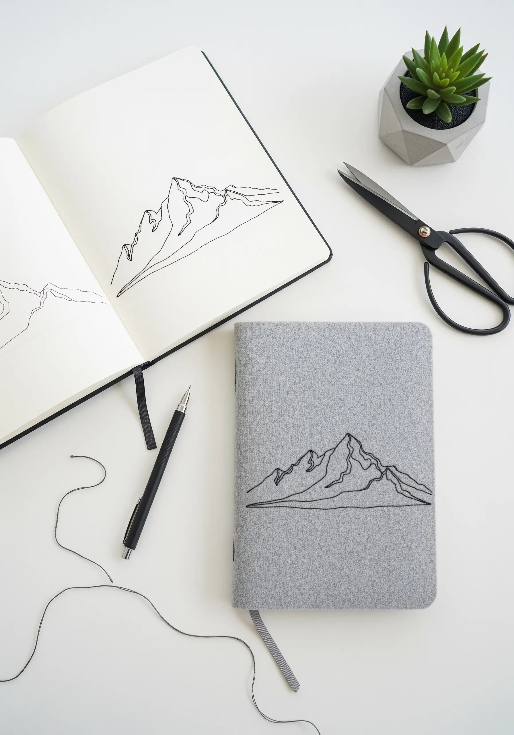 A minimalist mountain range embroidered with black thread onto the grey fabric cover of a journal.