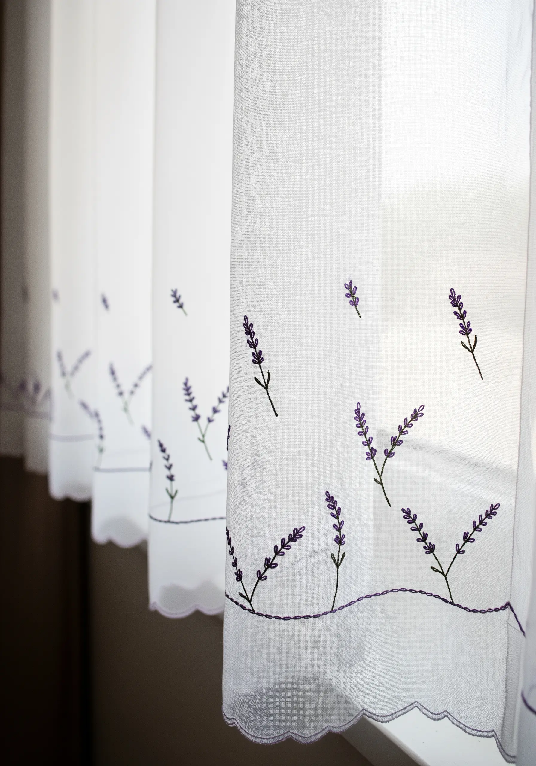 Delicate lavender sprigs embroidered along the scalloped hem of sheer white curtains.
