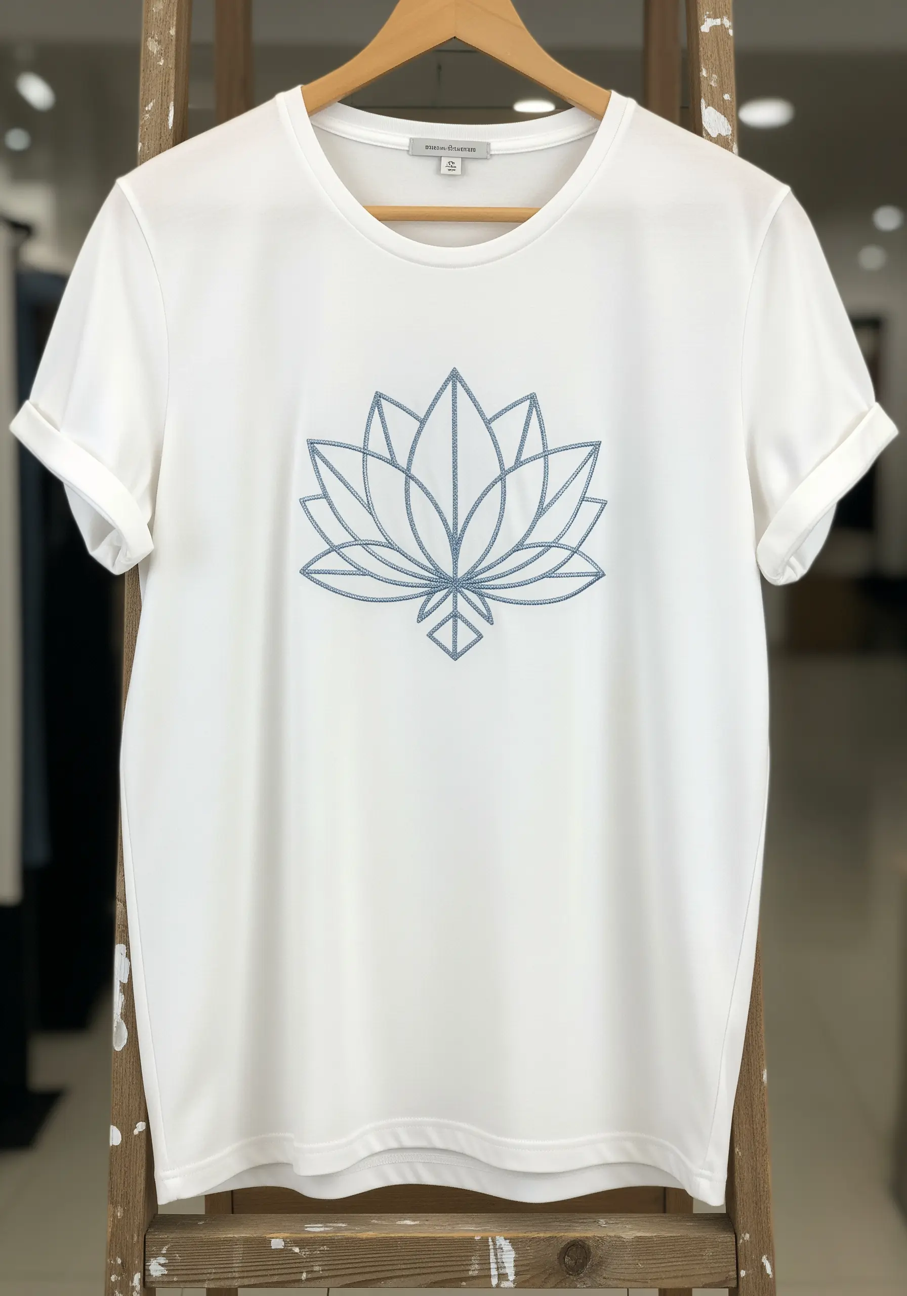 Geometric lotus flower embroidered in blue-gray thread on a white t-shirt.