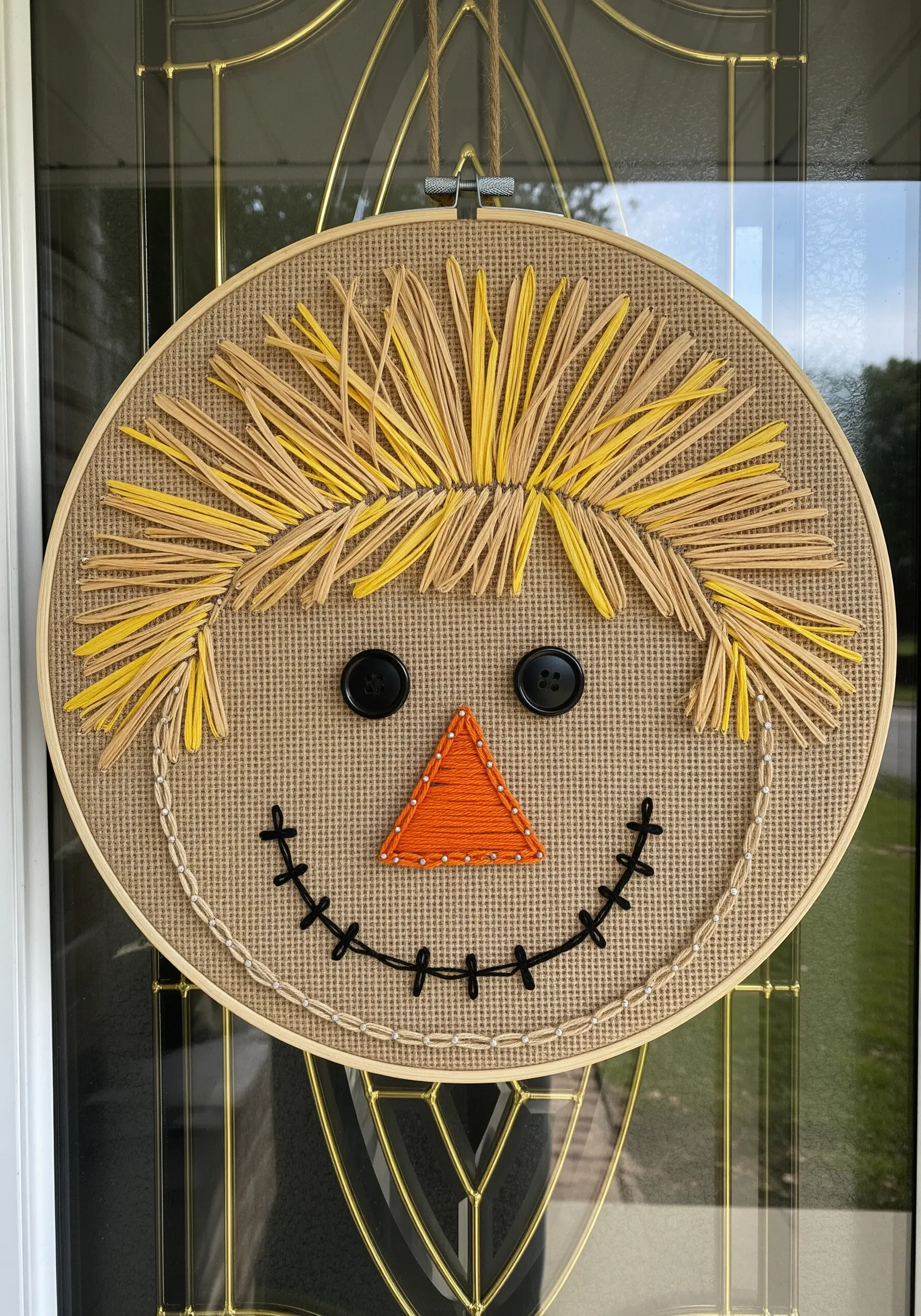 Rustic scarecrow face hoop art using raffia for hair and black button eyes.