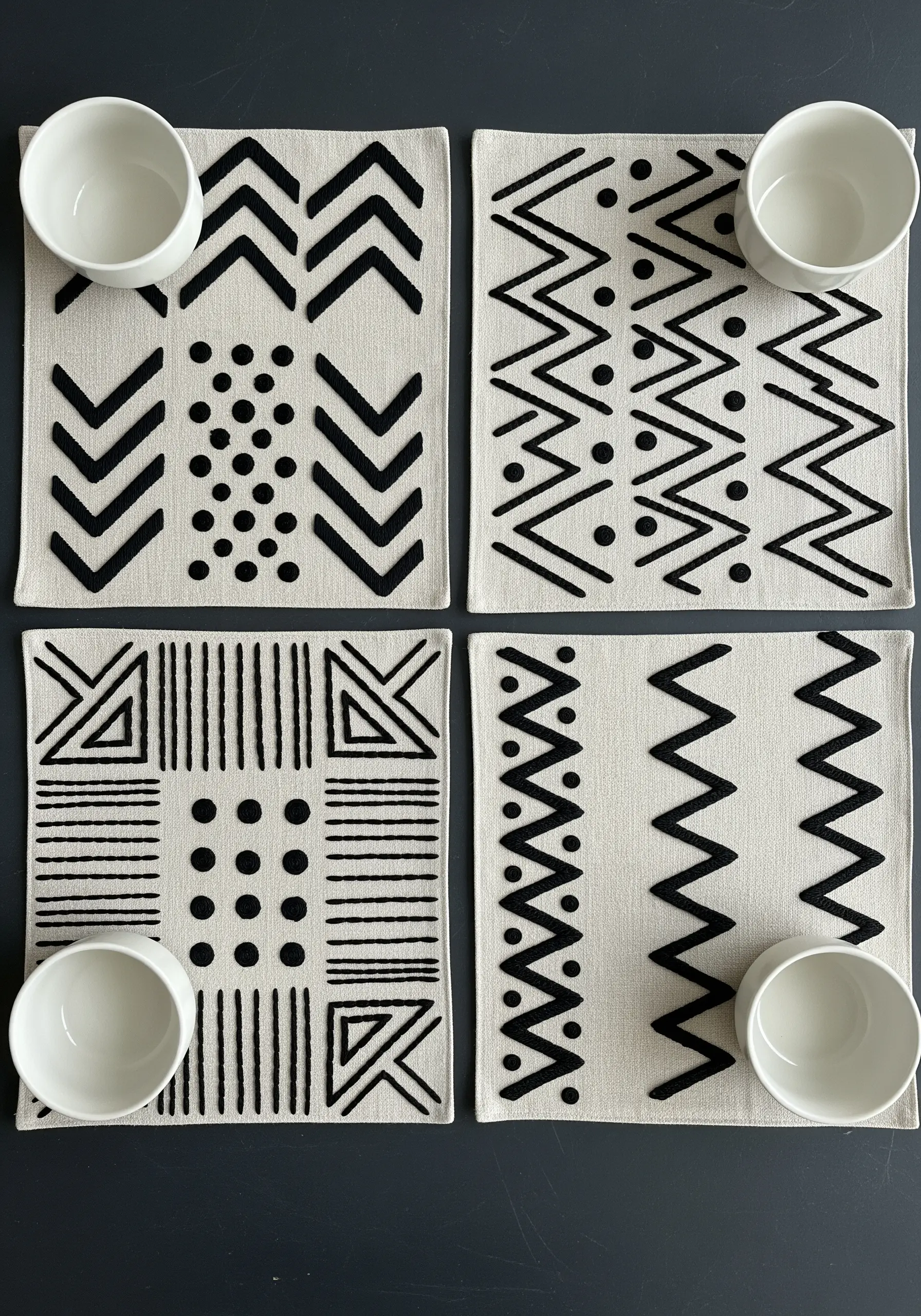 Four neutral placemats with bold, black geometric patterns created with dense satin stitch.