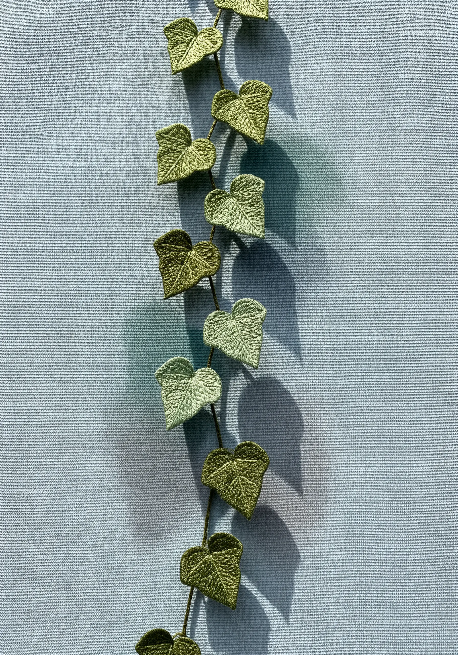 A vine of 3D embroidered ivy leaves lifting off a blue fabric, creating real shadows.