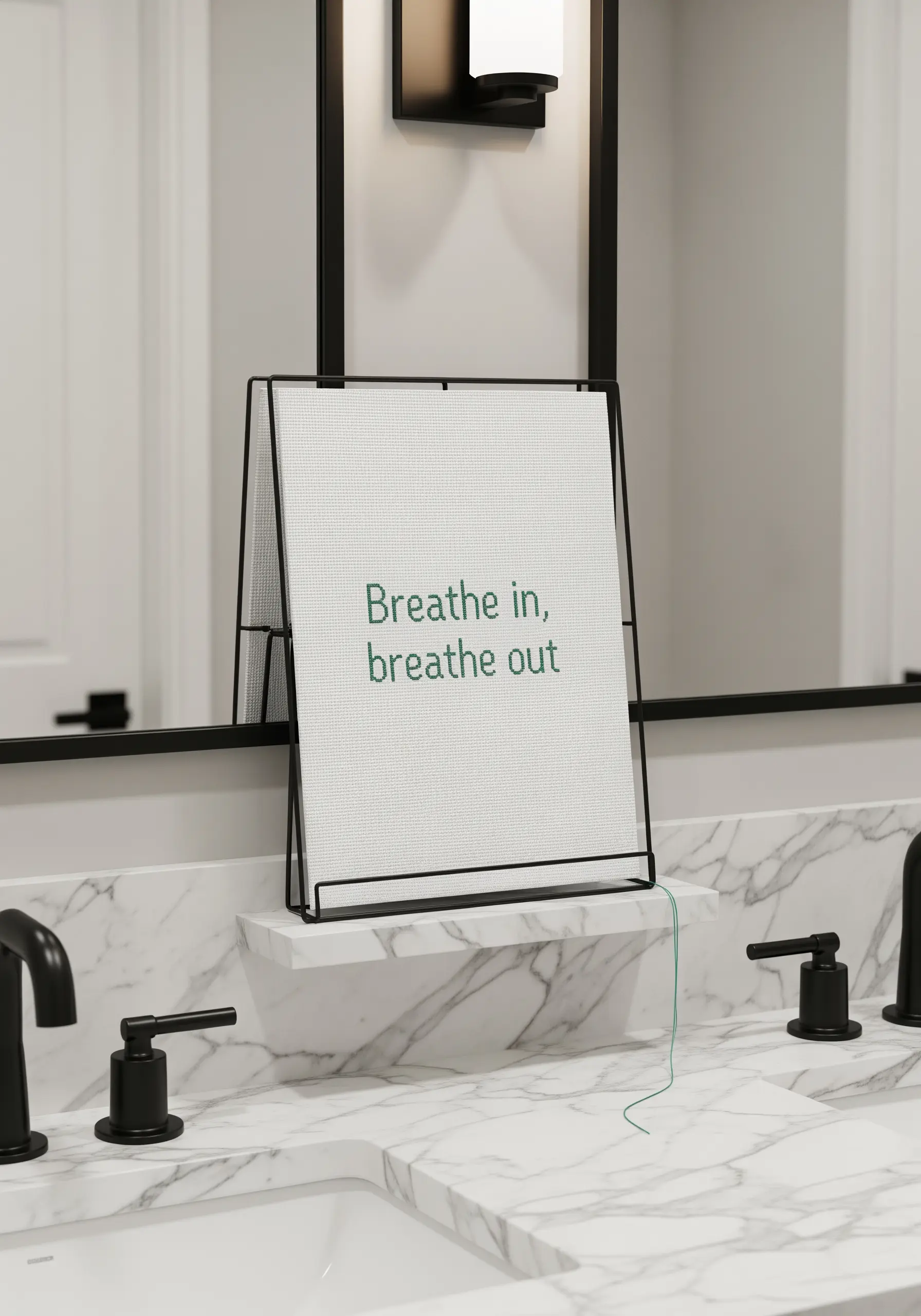 A minimalist embroidered quote on white fabric, displayed on a modern black stand.