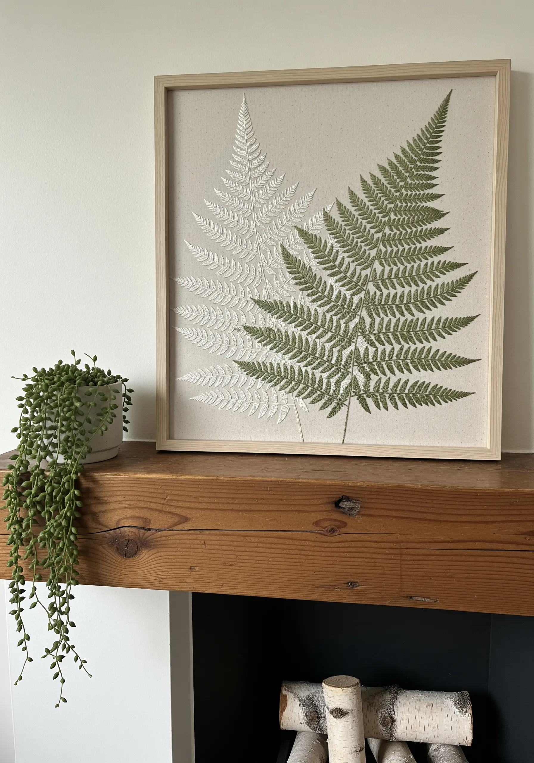 Framed embroidery of two fern leaves, one in white and one in green.