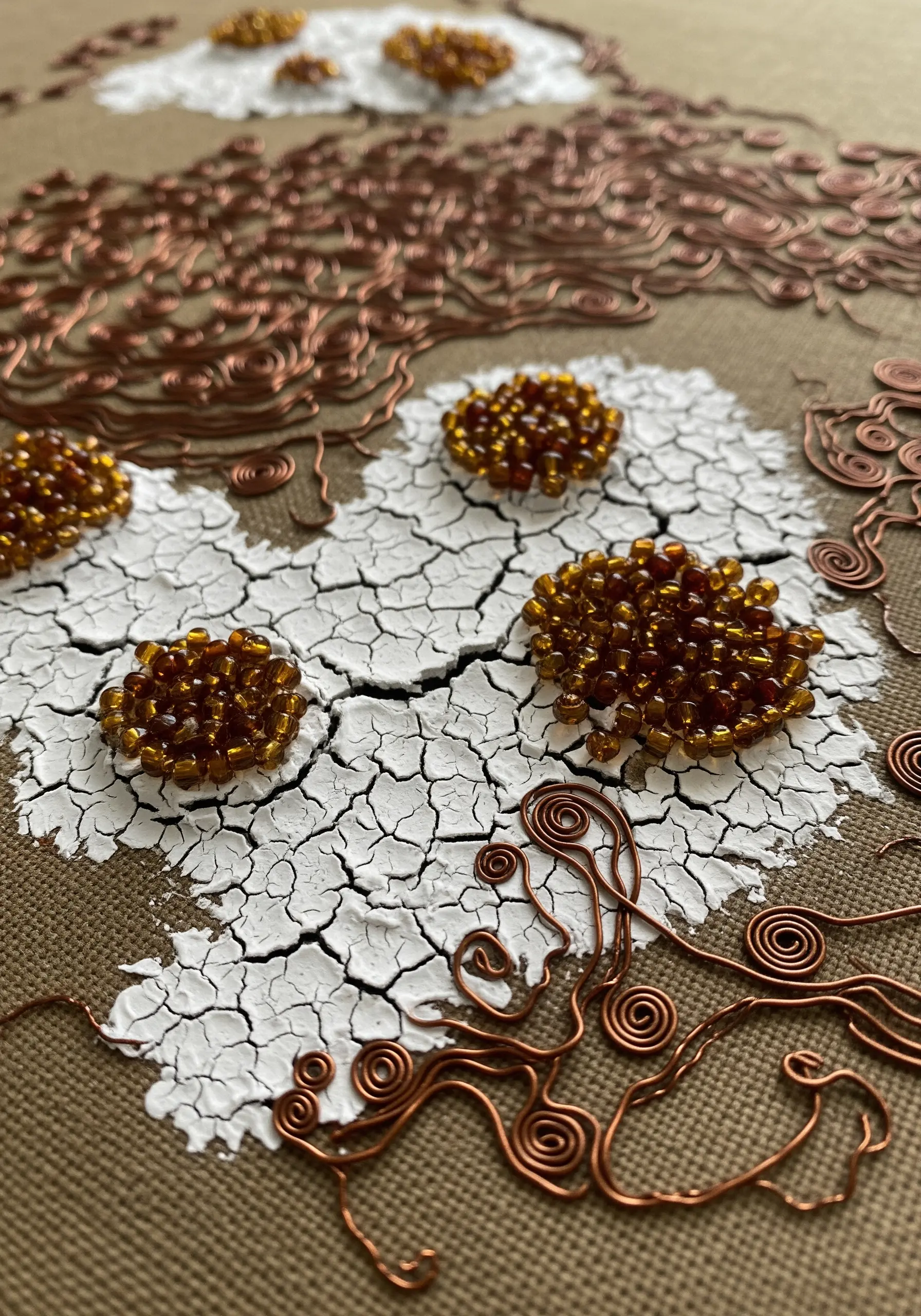 Detail of crackle paint effect on fabric with copper wire swirls and beaded flower centers.