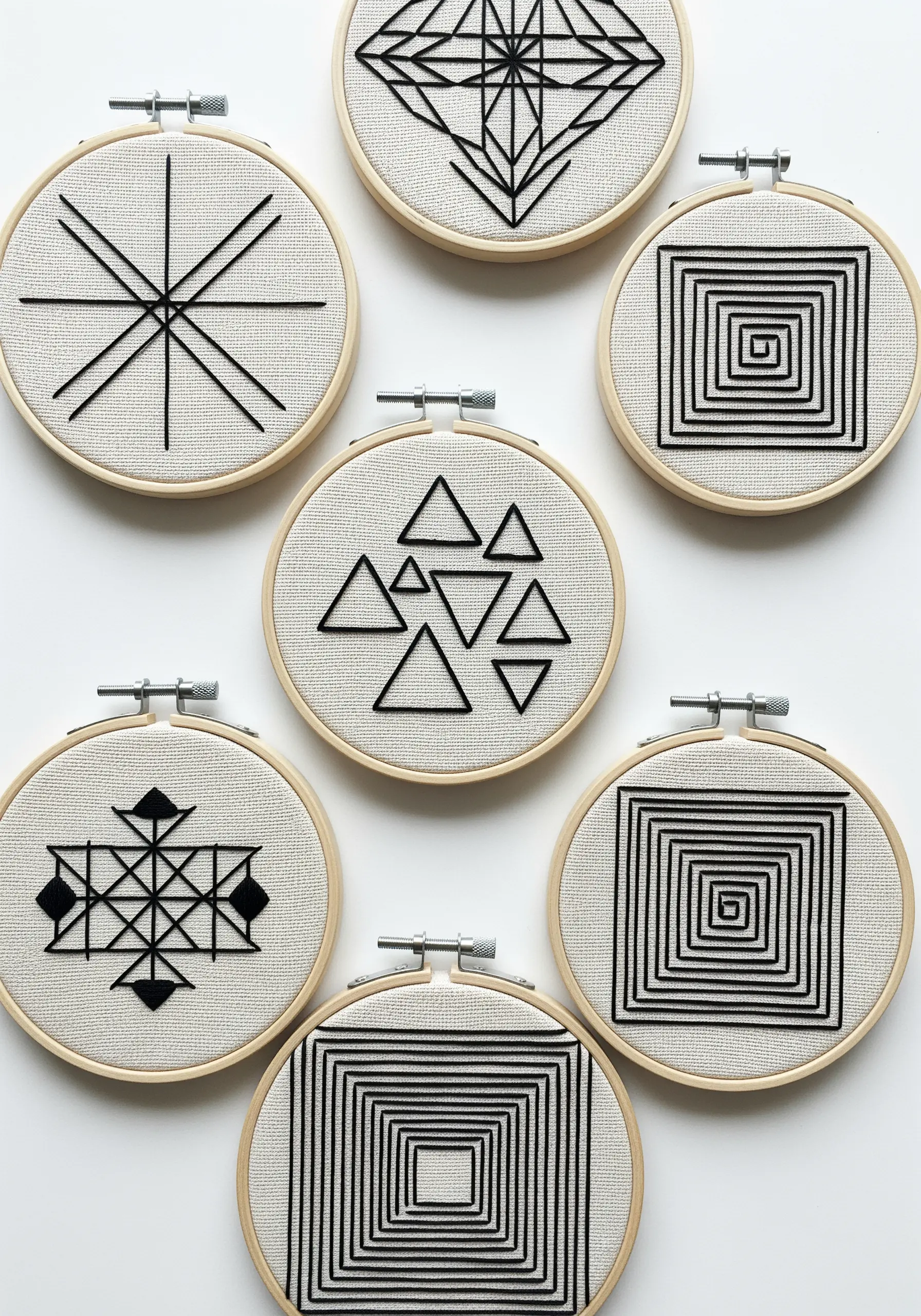 A collection of small embroidery hoops featuring minimalist geometric blackwork patterns.