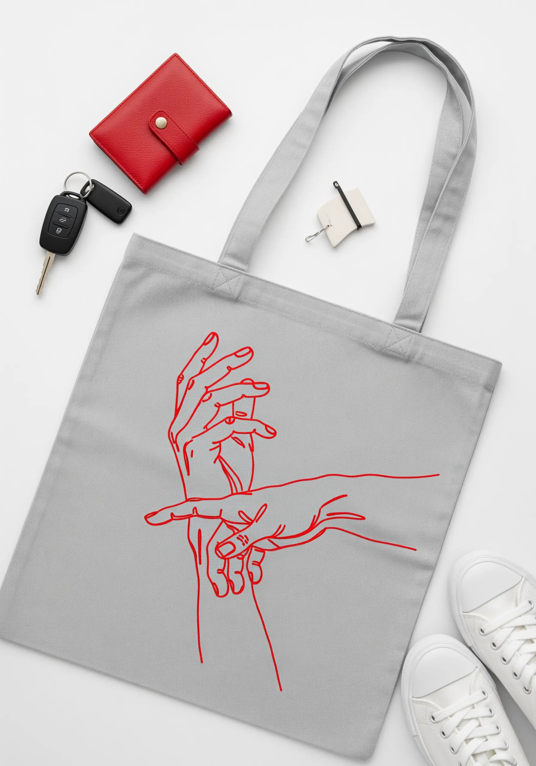 Interlocking hands outlined in vibrant red thread on a light grey tote bag.