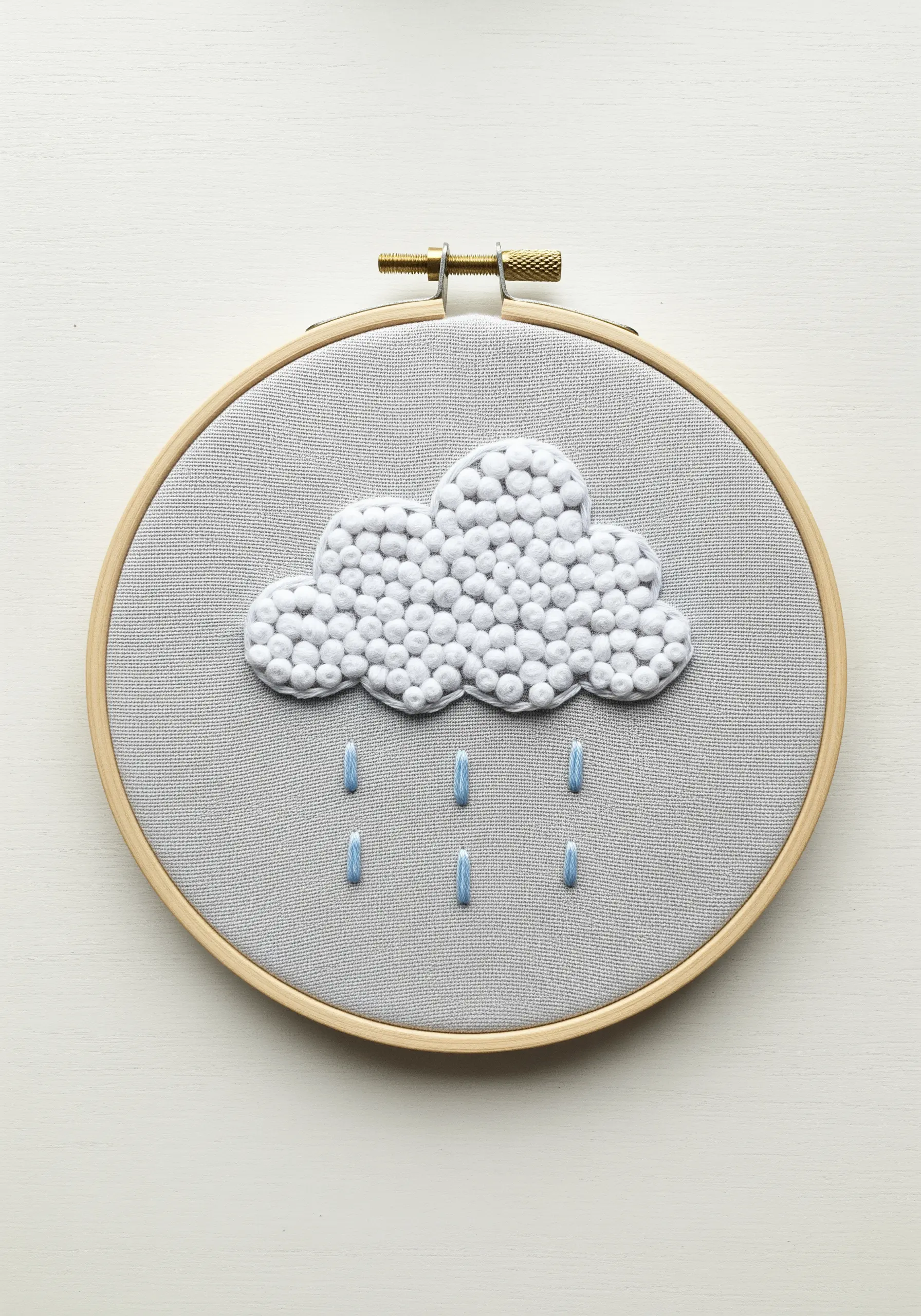 A fluffy cloud embroidered with dense white French knots and blue satin stitch raindrops.