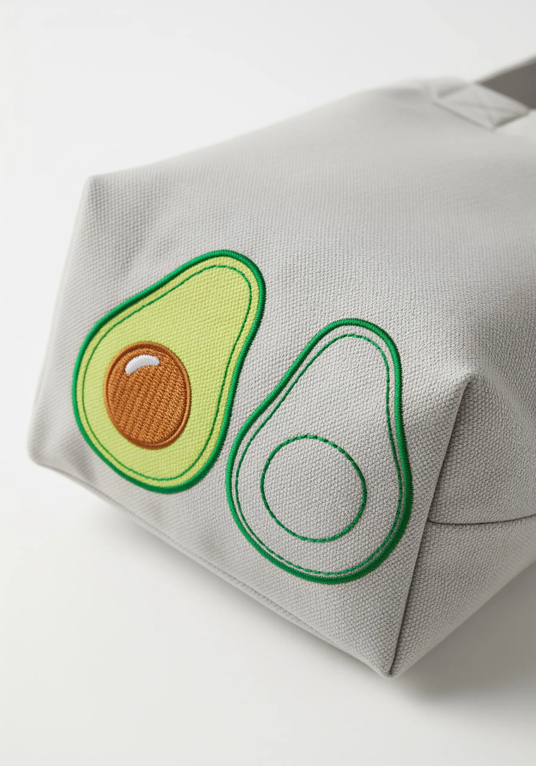 One filled and one outlined embroidered avocado on the side of a grey canvas bag.