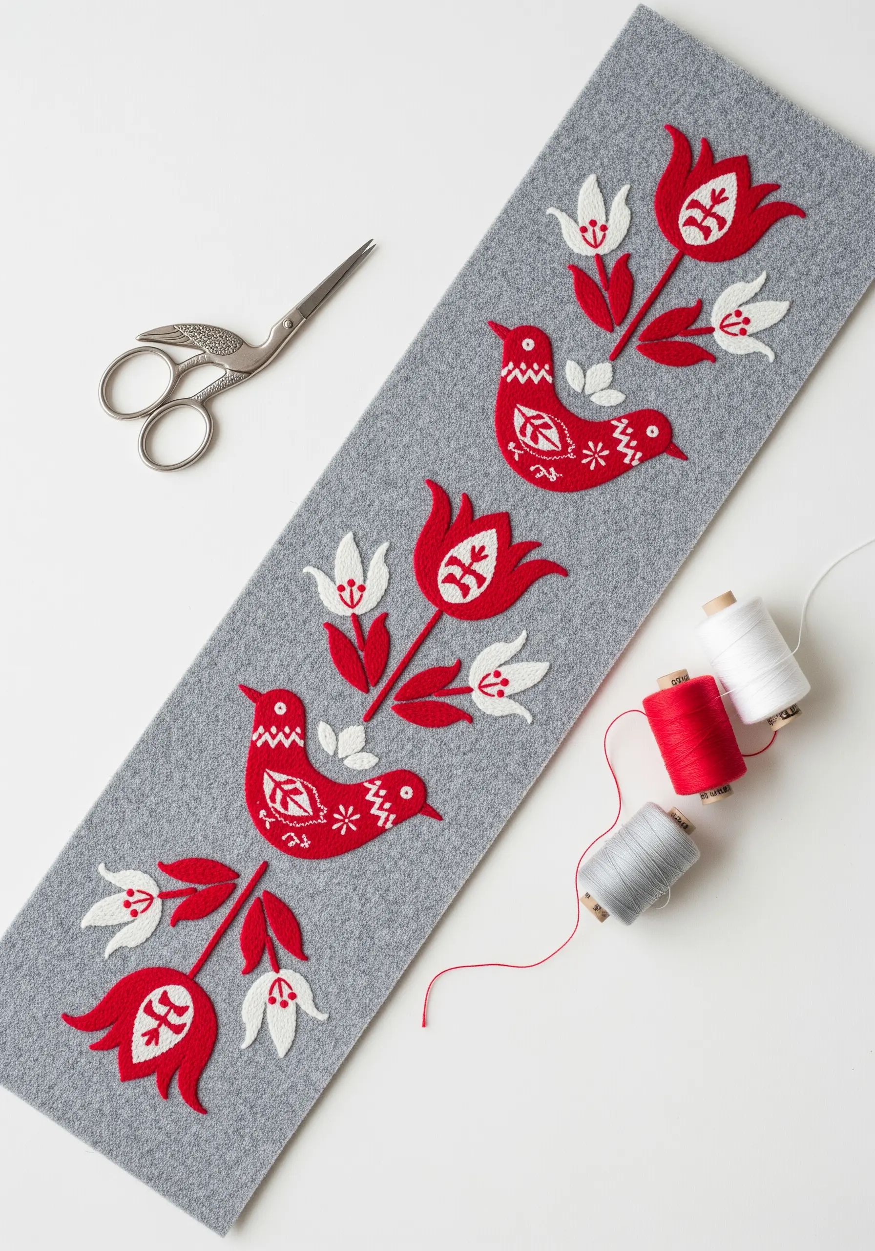A grey felt table runner decorated with red and white folk art appliqué birds and tulips.