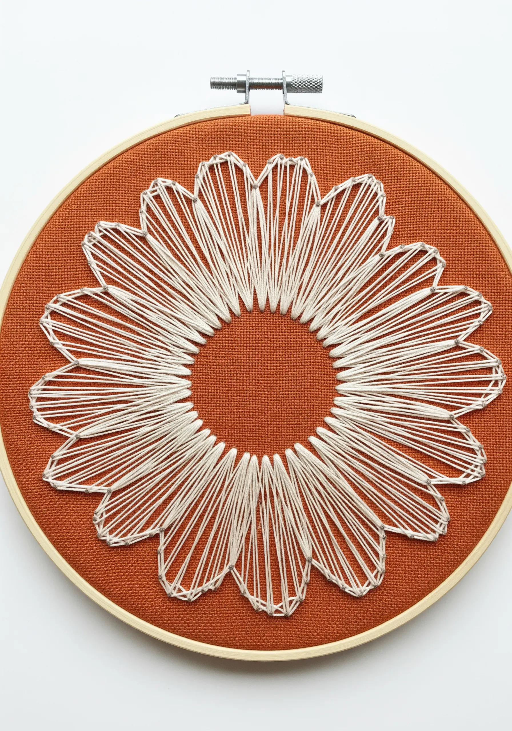 Hoop art of a daisy with white thread petals on a burnt orange fabric background