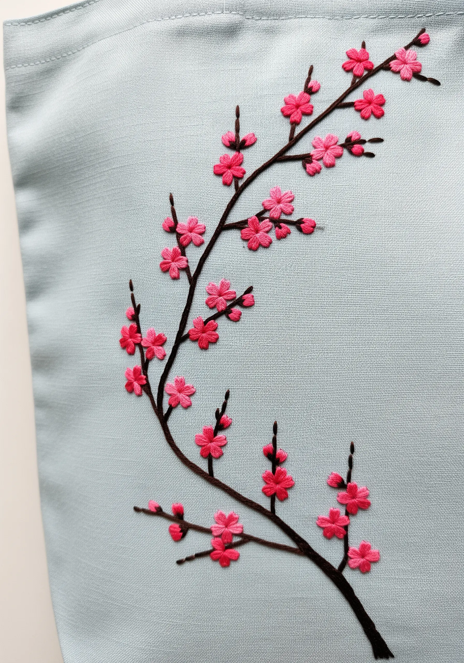 A cherry blossom branch with pink lazy daisy stitch flowers on a light blue tote bag.