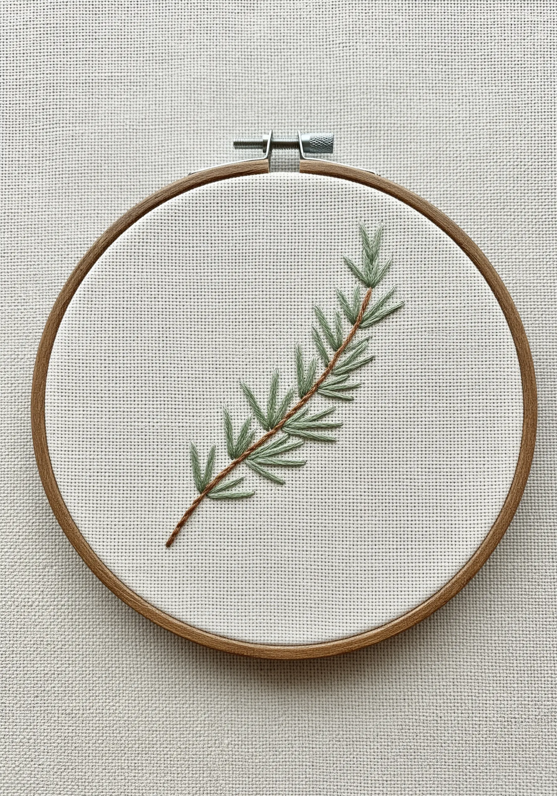 A single sprig of rosemary embroidered on Aida cloth using fly stitch for the leaves.