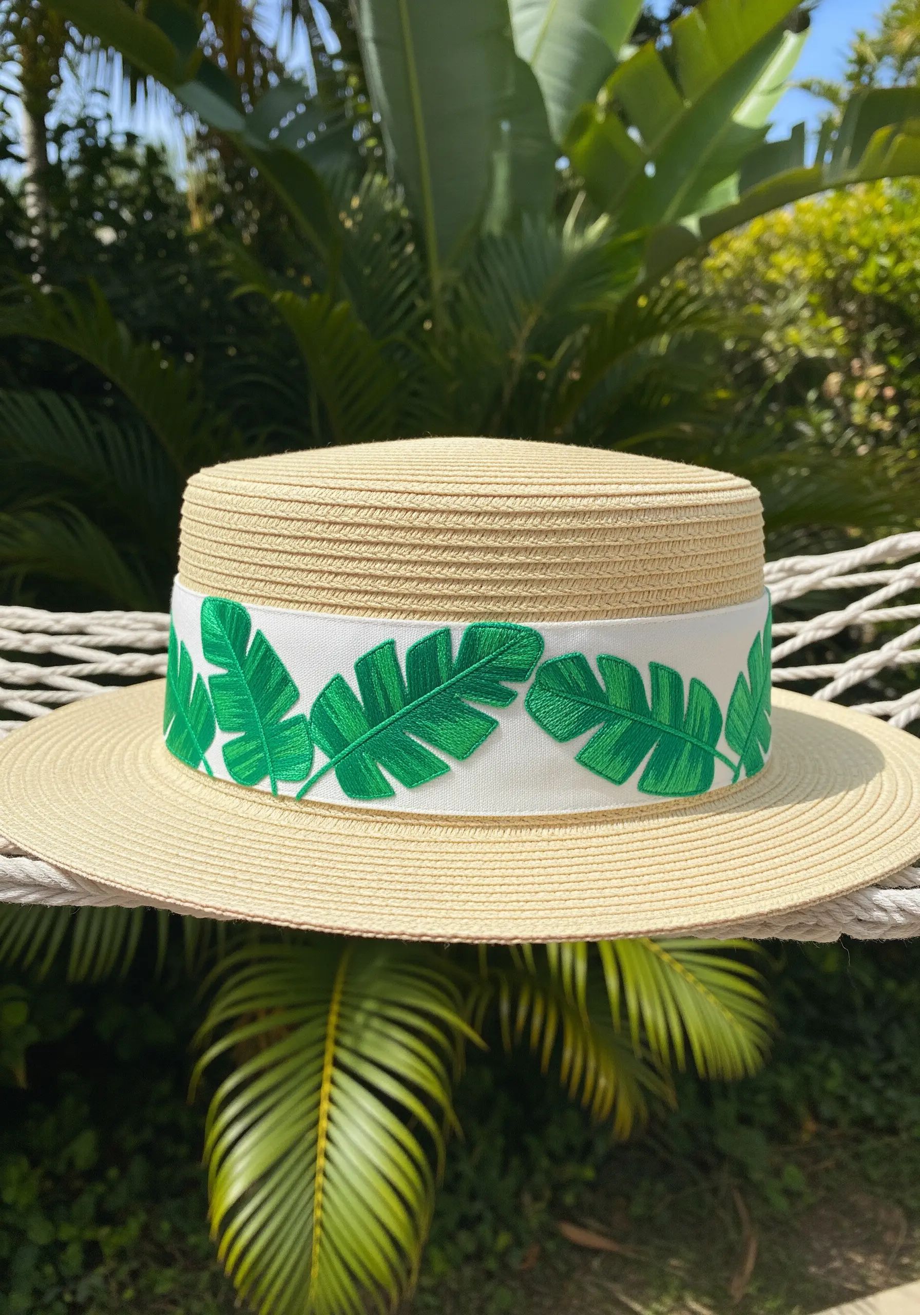 Bold green banana leaves embroidered on a white band around a straw boater hat.