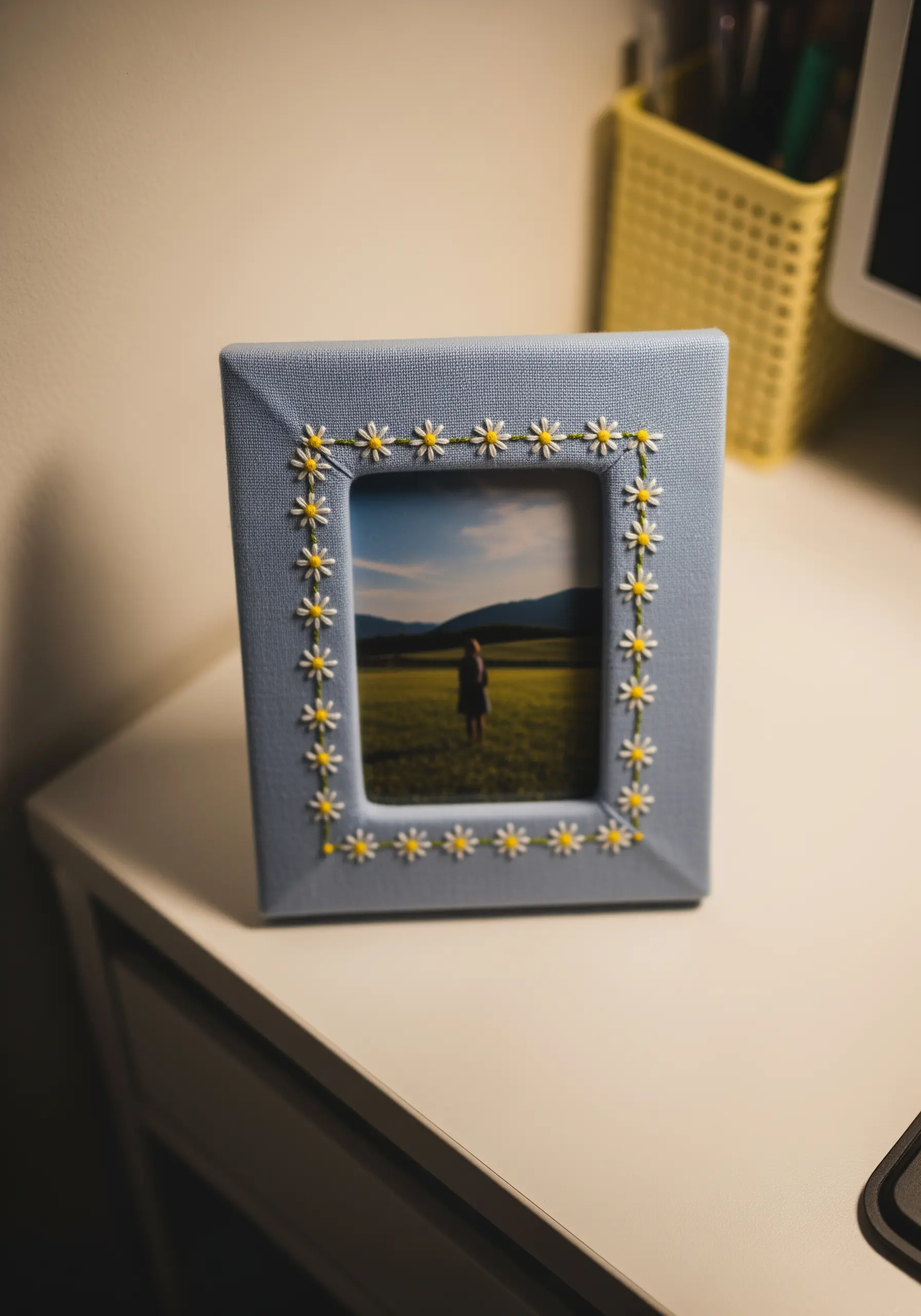 A hand-stitched border of daisies around the opening of a fabric photo frame