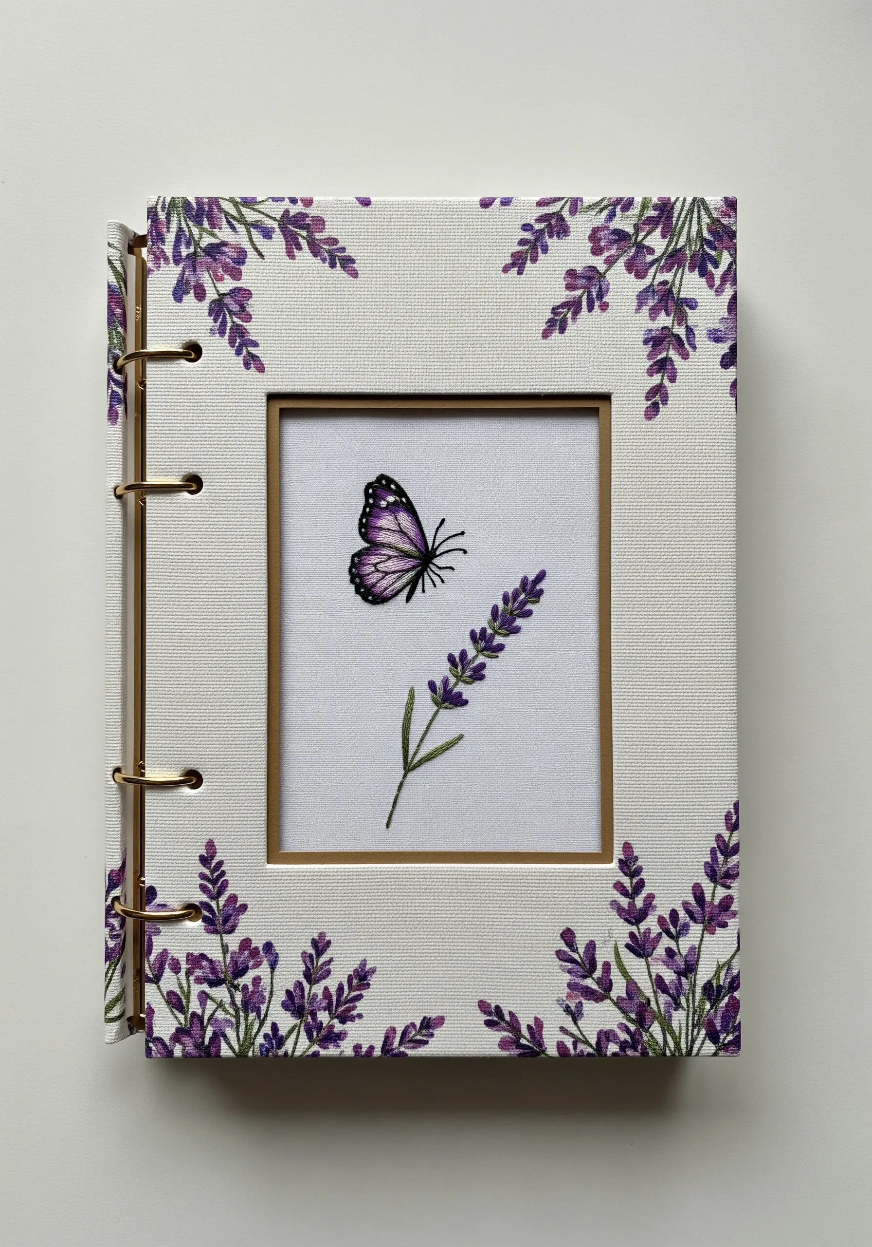 An embroidered lavender sprig and butterfly displayed in the cutout window of a photo album.