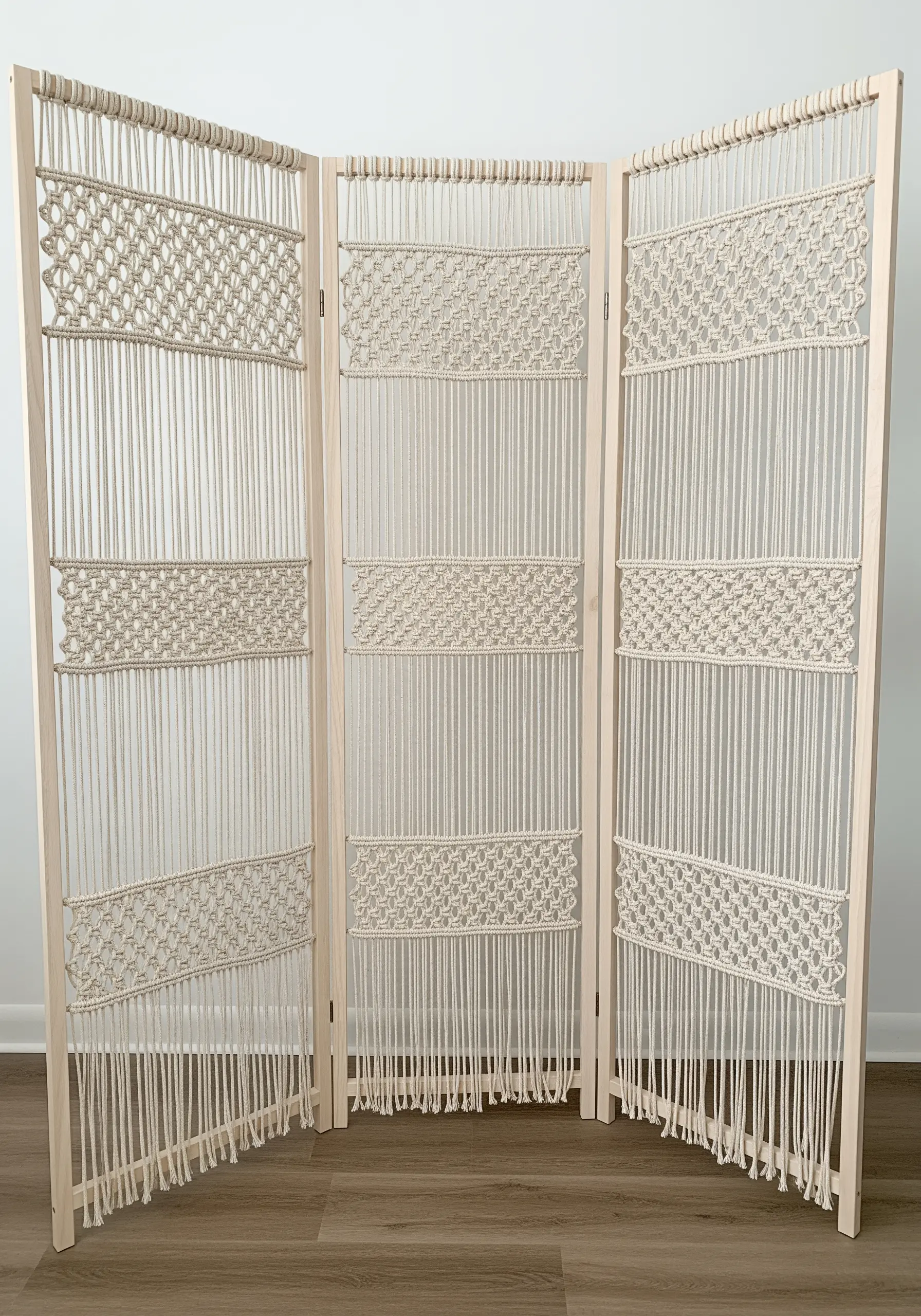 A three-panel macramé room divider with geometric knotted patterns and long fringe.