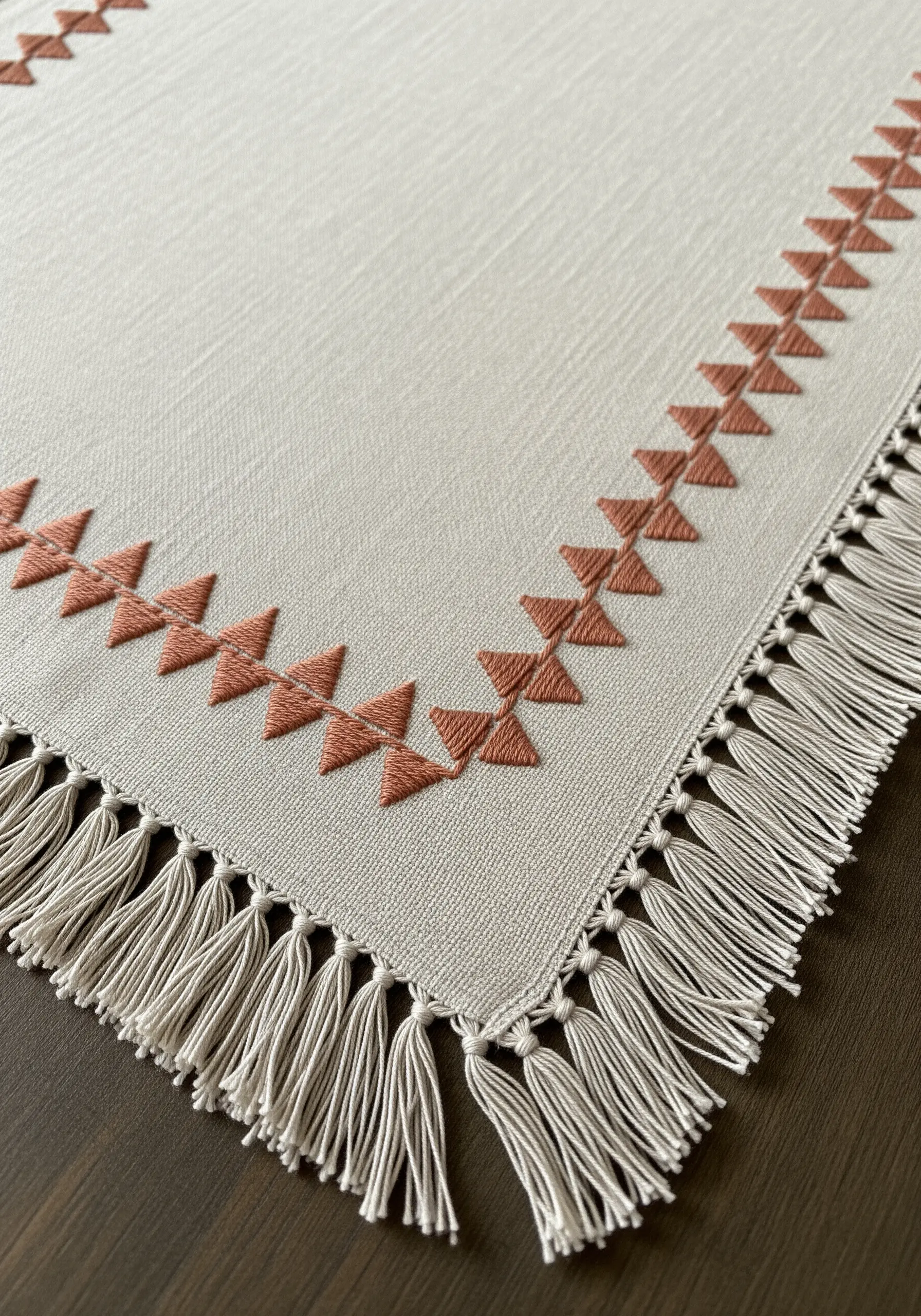 A geometric border of terracotta-colored triangles on a cream table runner with a fringed edge.