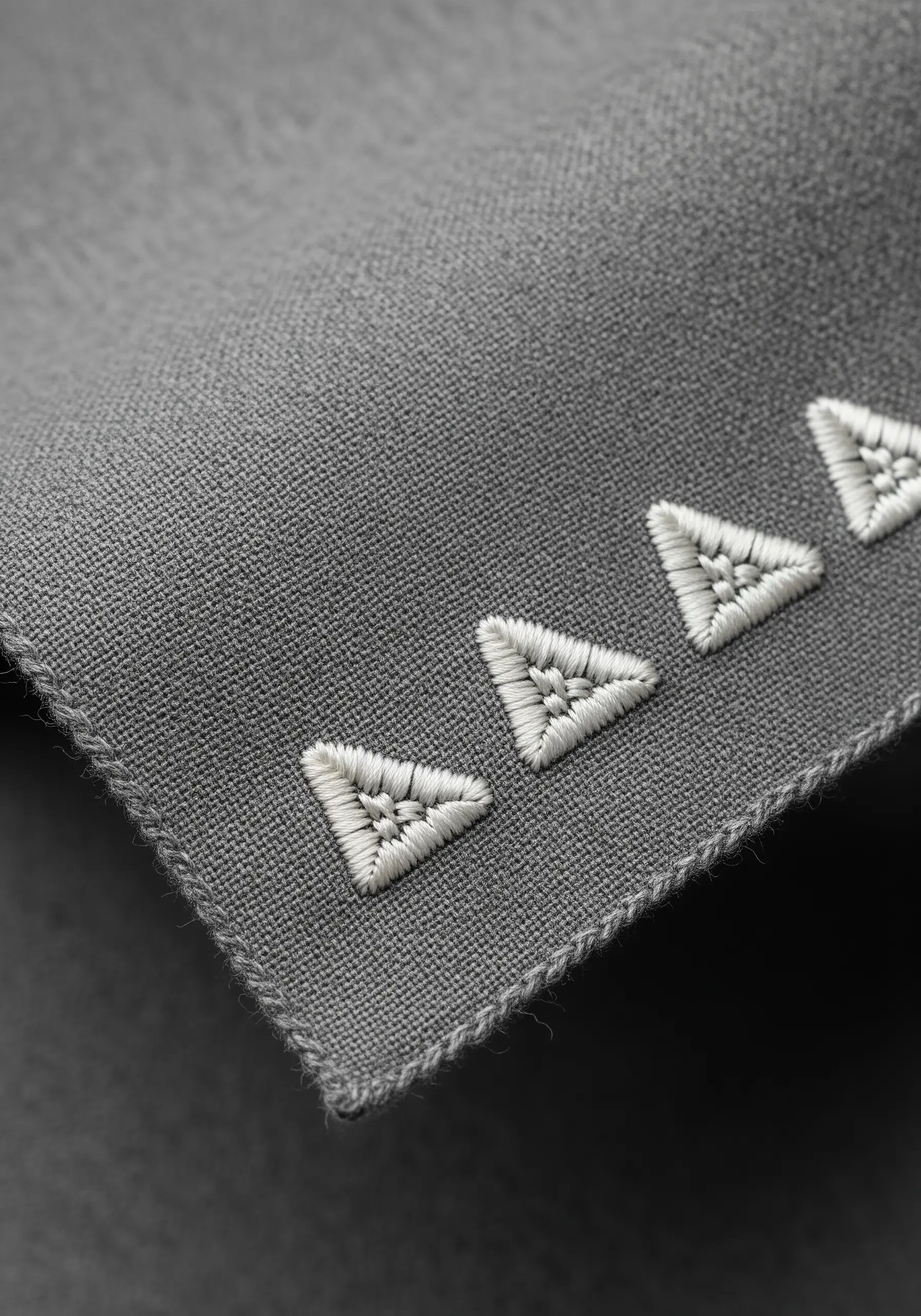 A row of four white geometric triangles with satin stitch fill on a grey scarf.