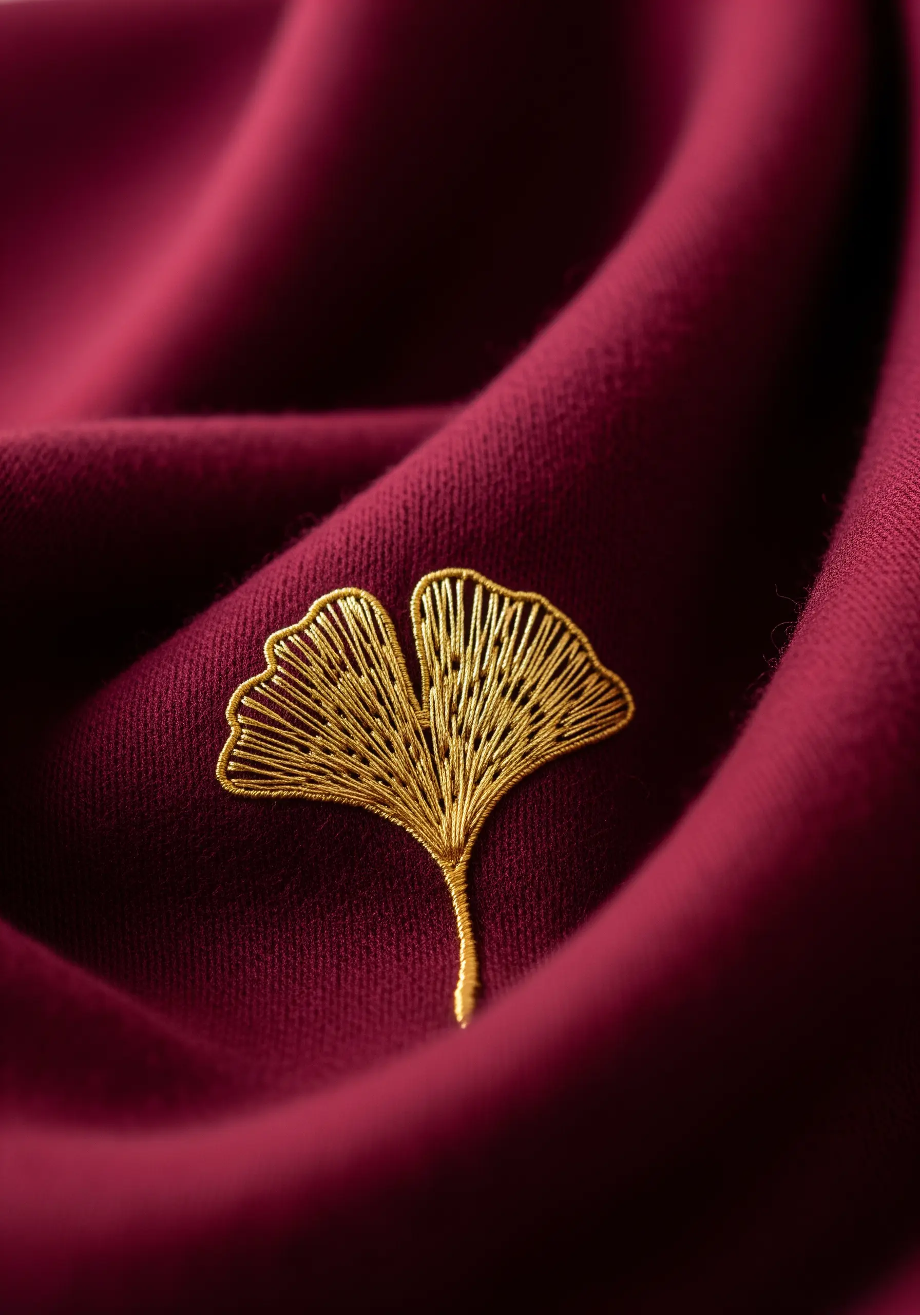 A golden metallic thread embroidery of a ginkgo leaf on a deep red scarf.