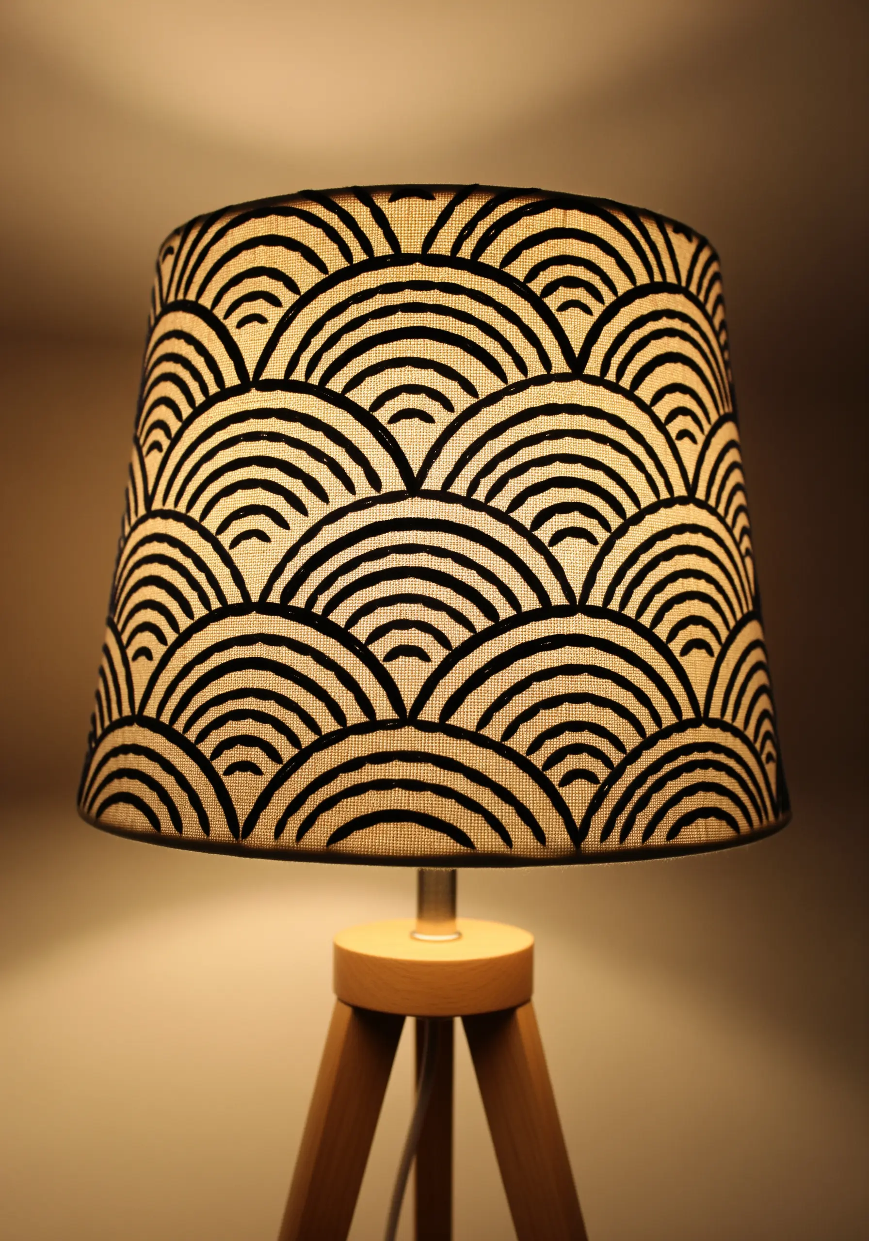 A linen lampshade embroidered with a repeating black geometric arch pattern, creating a silhouette effect.