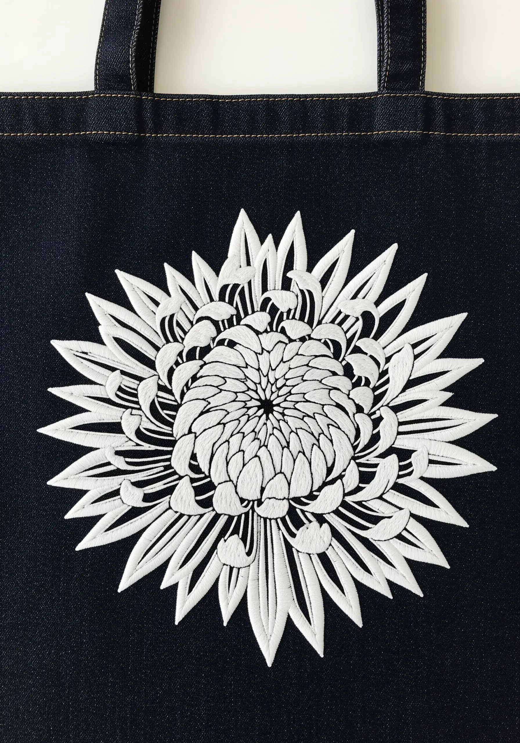 A high-contrast white chrysanthemum embroidered on a dark denim tote bag.