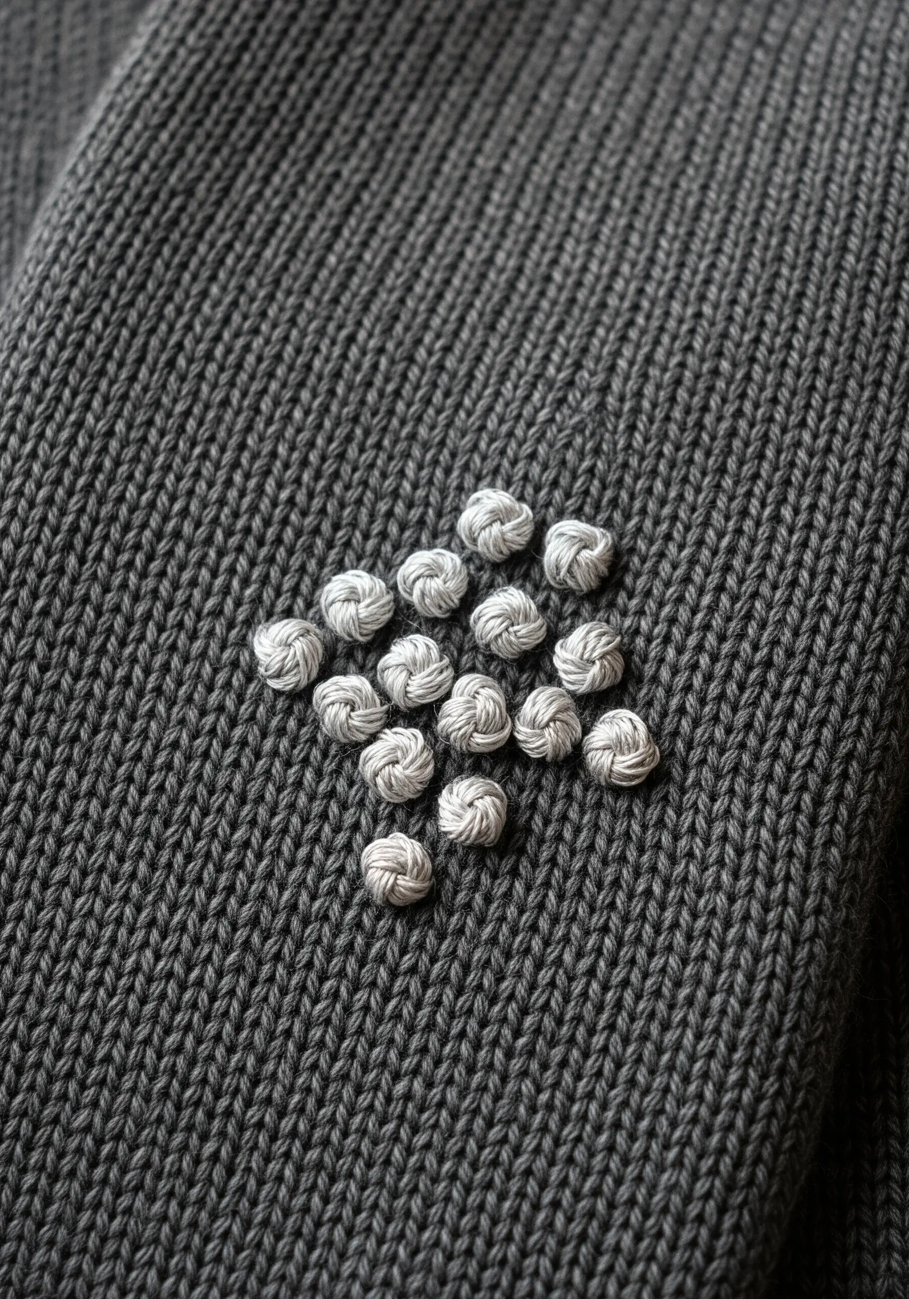 A diamond shape filled with a grid of small white knots on a dark grey knit scarf.