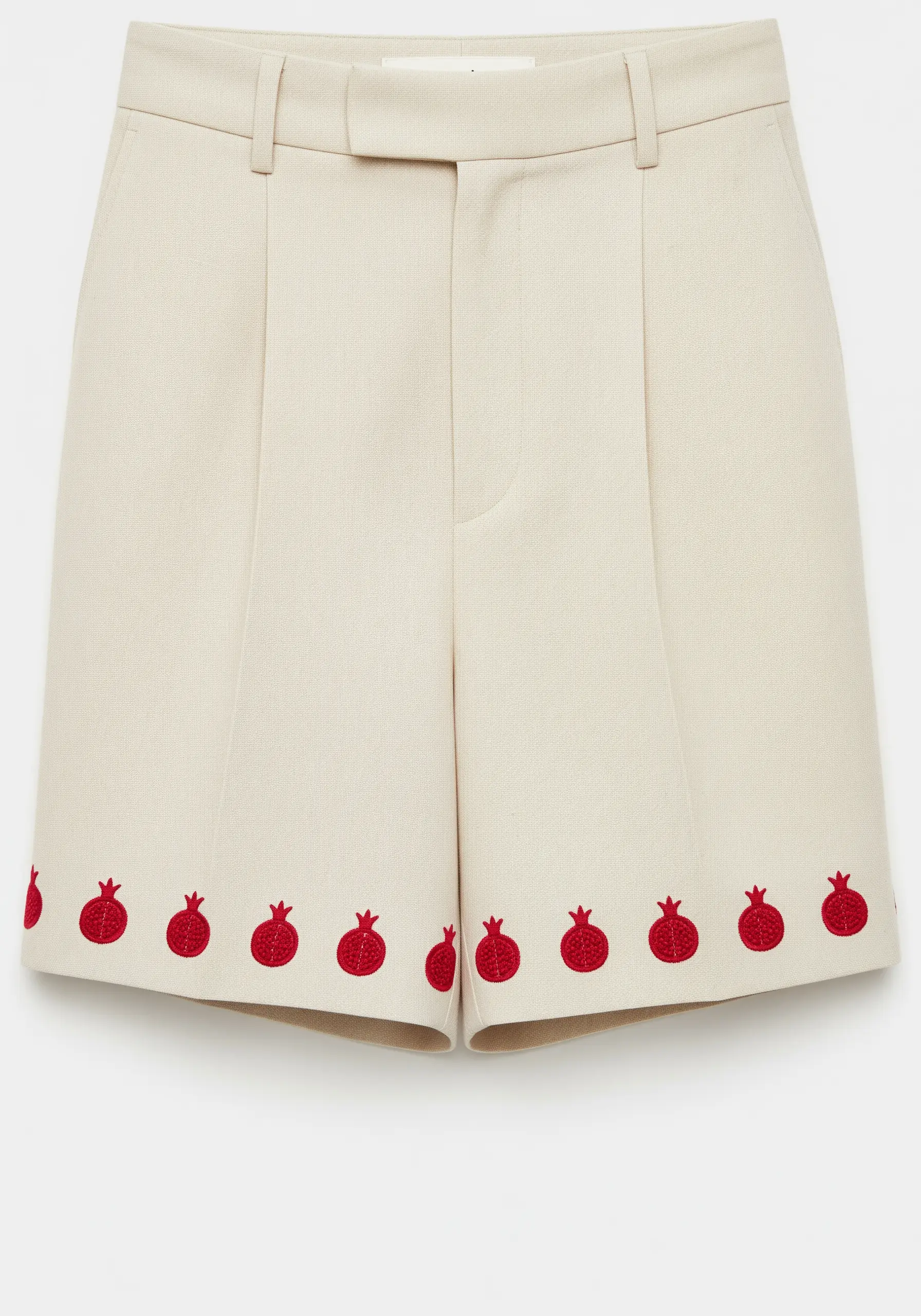A repeating border of small red pomegranates embroidered along the hem of cream shorts.