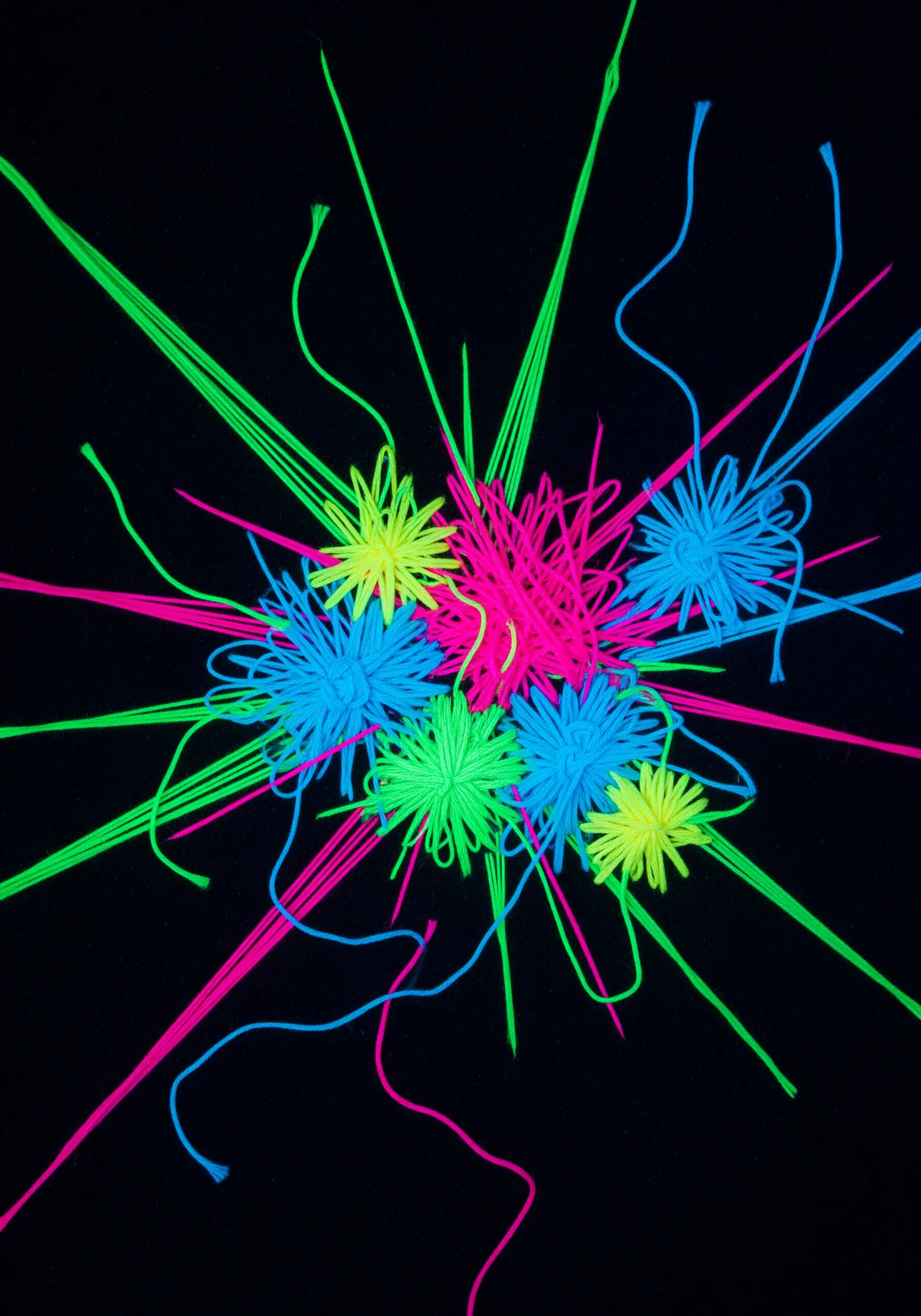 Bright neon pink, green, yellow, and blue threads create starburst shapes on black fabric.
