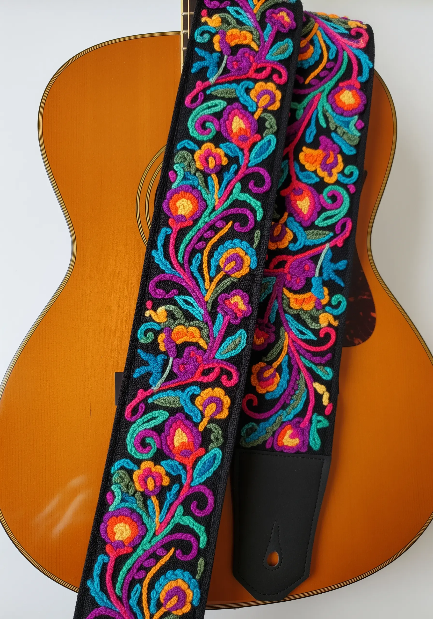 A vibrant, densely embroidered floral guitar strap with bold jewel tones on a black background.