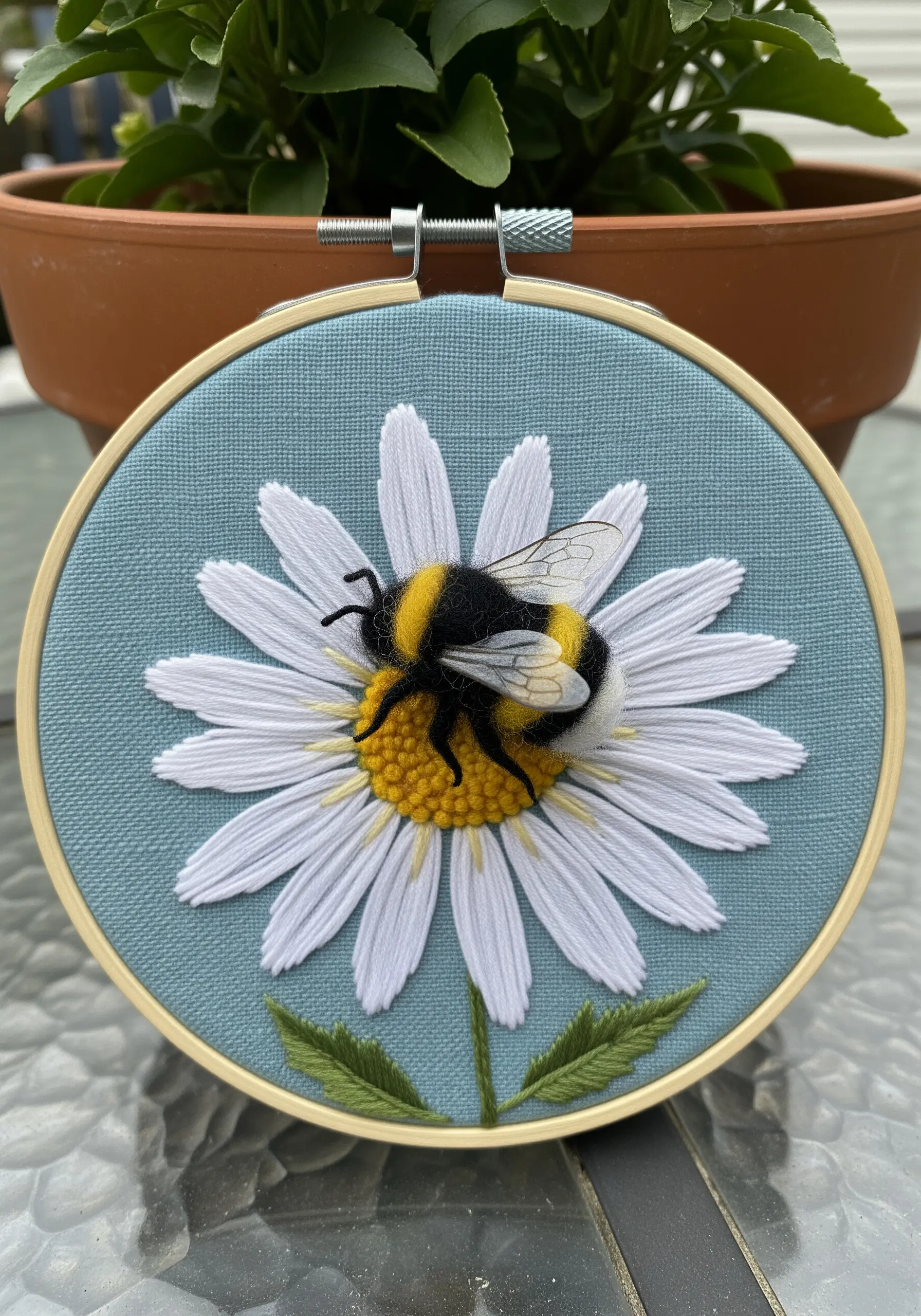 A dimensional embroidery of a bumblebee on a daisy, with a fuzzy felted body.